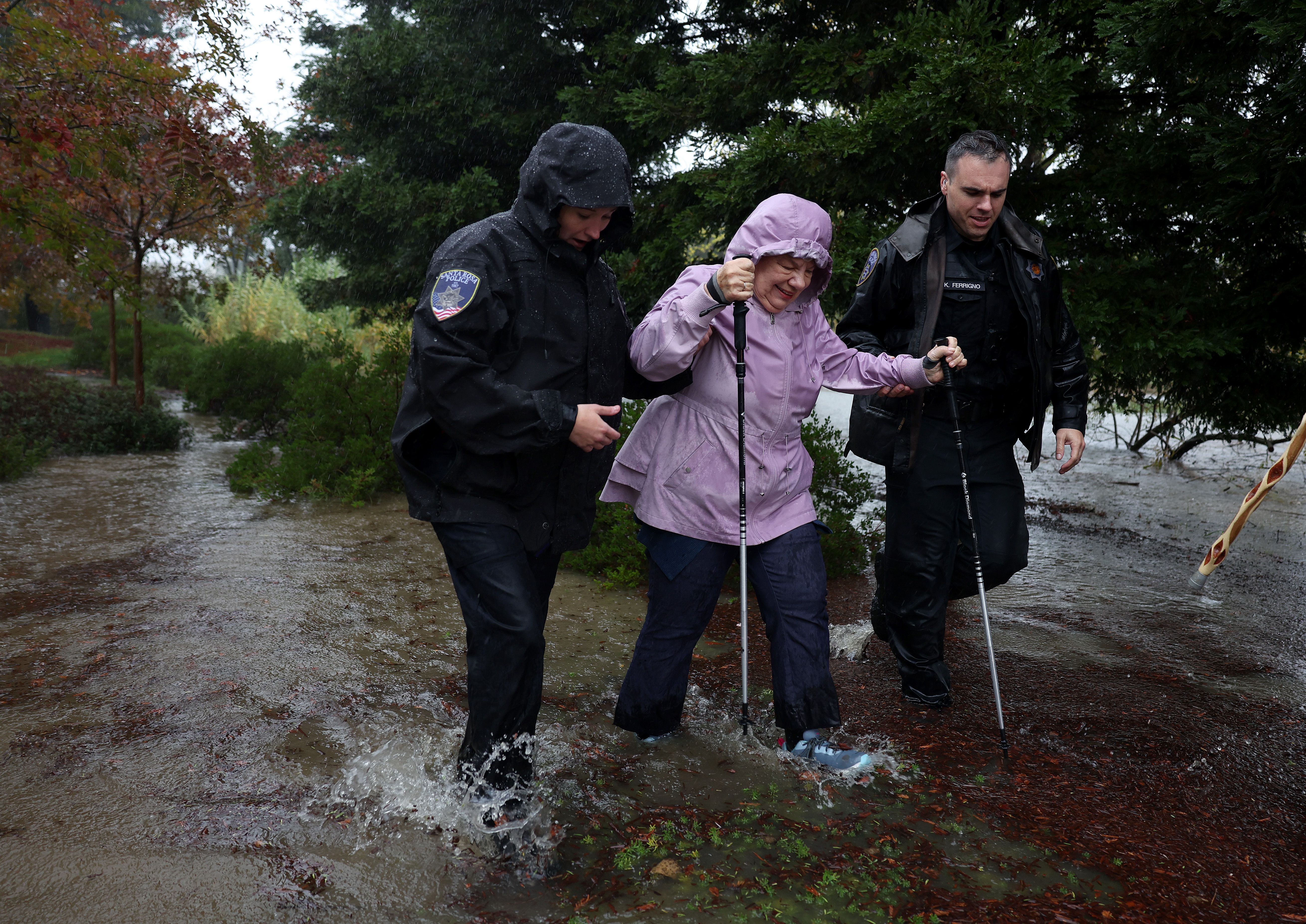 Santa Rosa police officers Ken Ferrigno (R) and Shannon Diana help an elderly woman walk through a flooded parking lot outside of Sutter Health on November 21, 2024, in Santa Rosa, California. 