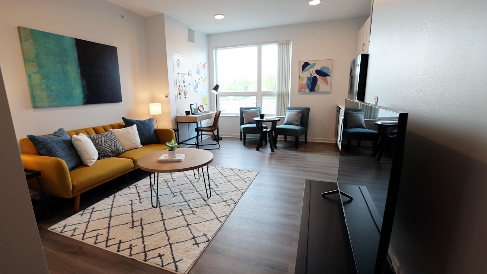 studio apartment with yellow couch, white rug, table and painting