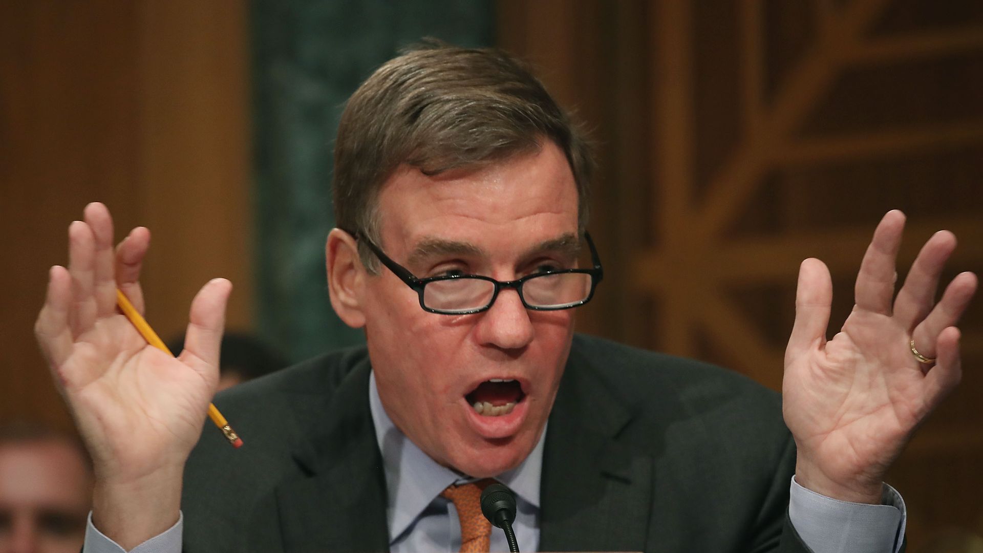 Mark Warner talks with hands up looking over glasses