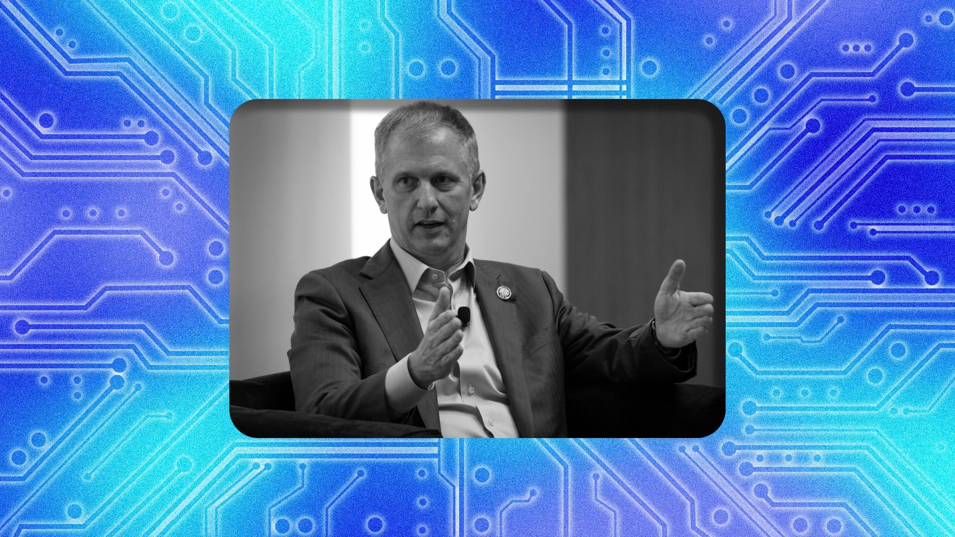 A grayscale photo of a man in a suit speaking, gesturing with his hands and wearing a lapel microphone, framed by a rounded border over a blue circuit-board pattern background.