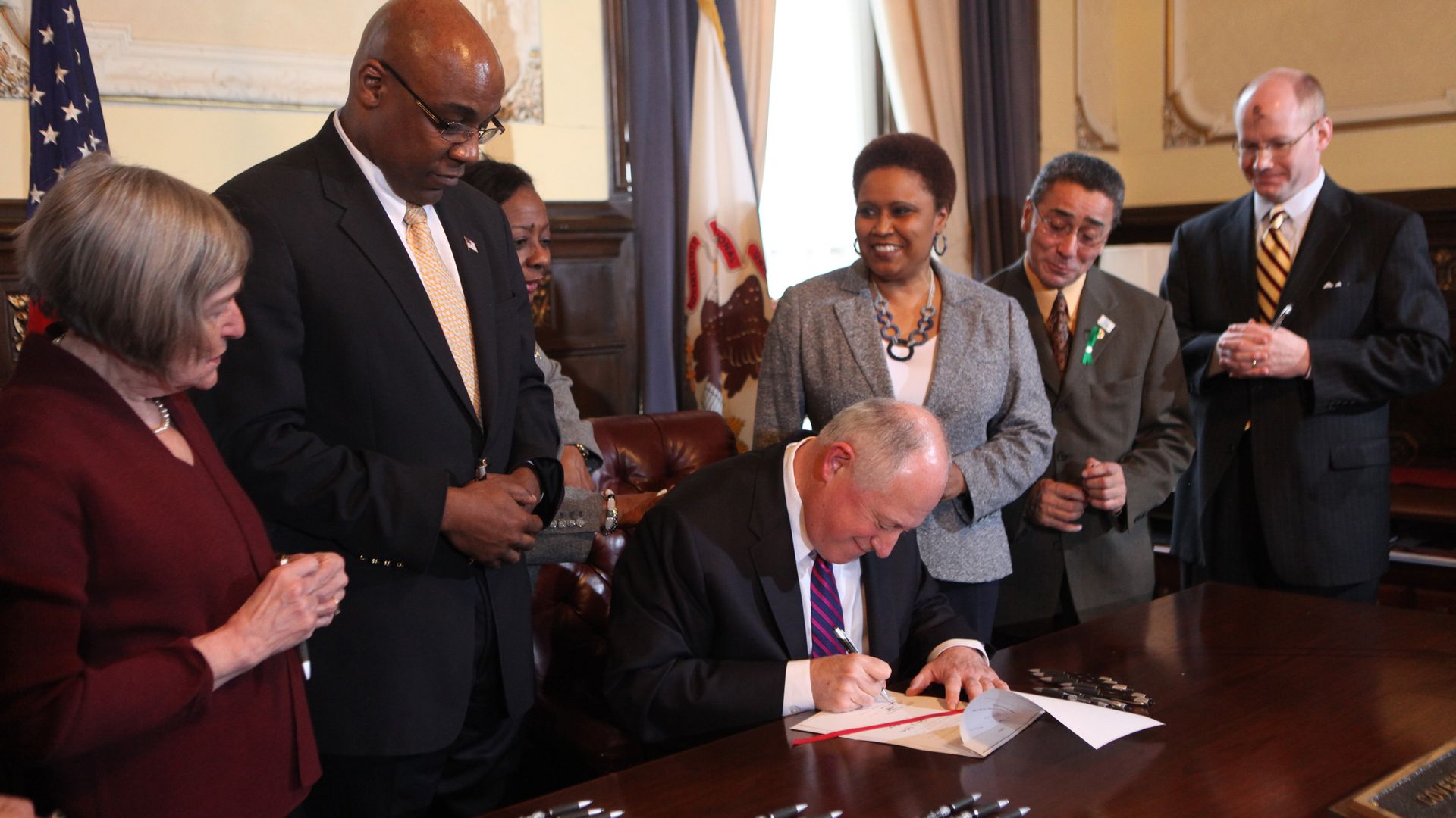 Photo of people standing around a man signing a document 