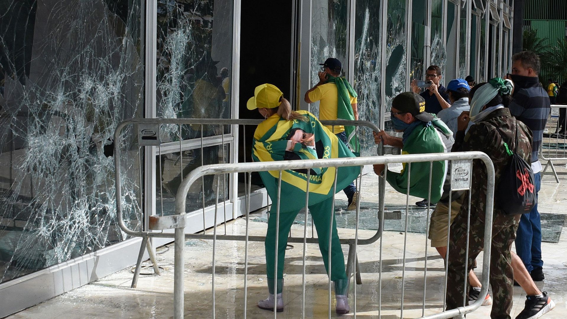 rioters in Brazil wearing Brazilian flags break large windows in Brasilia