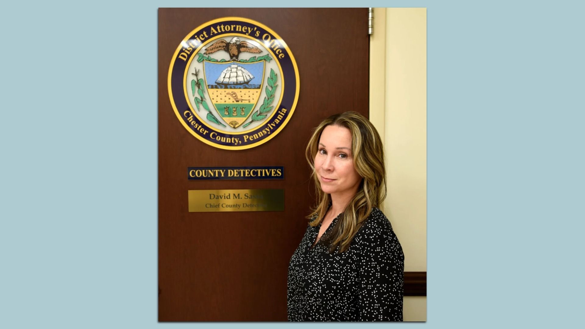 Pictured: Former Chester County Detective Christine Bleiler standing in front of a Chester County, Pennsylvania District Attorney's Office seal and sign reading "County Detectives."