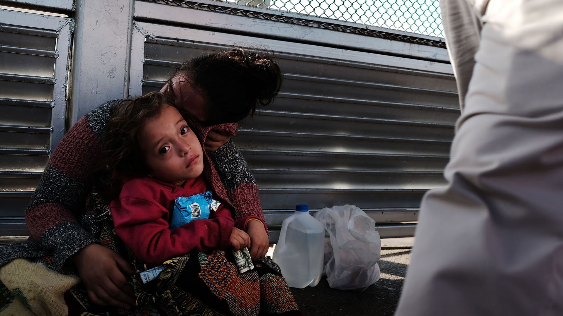A child and her mother sit in front of a fence