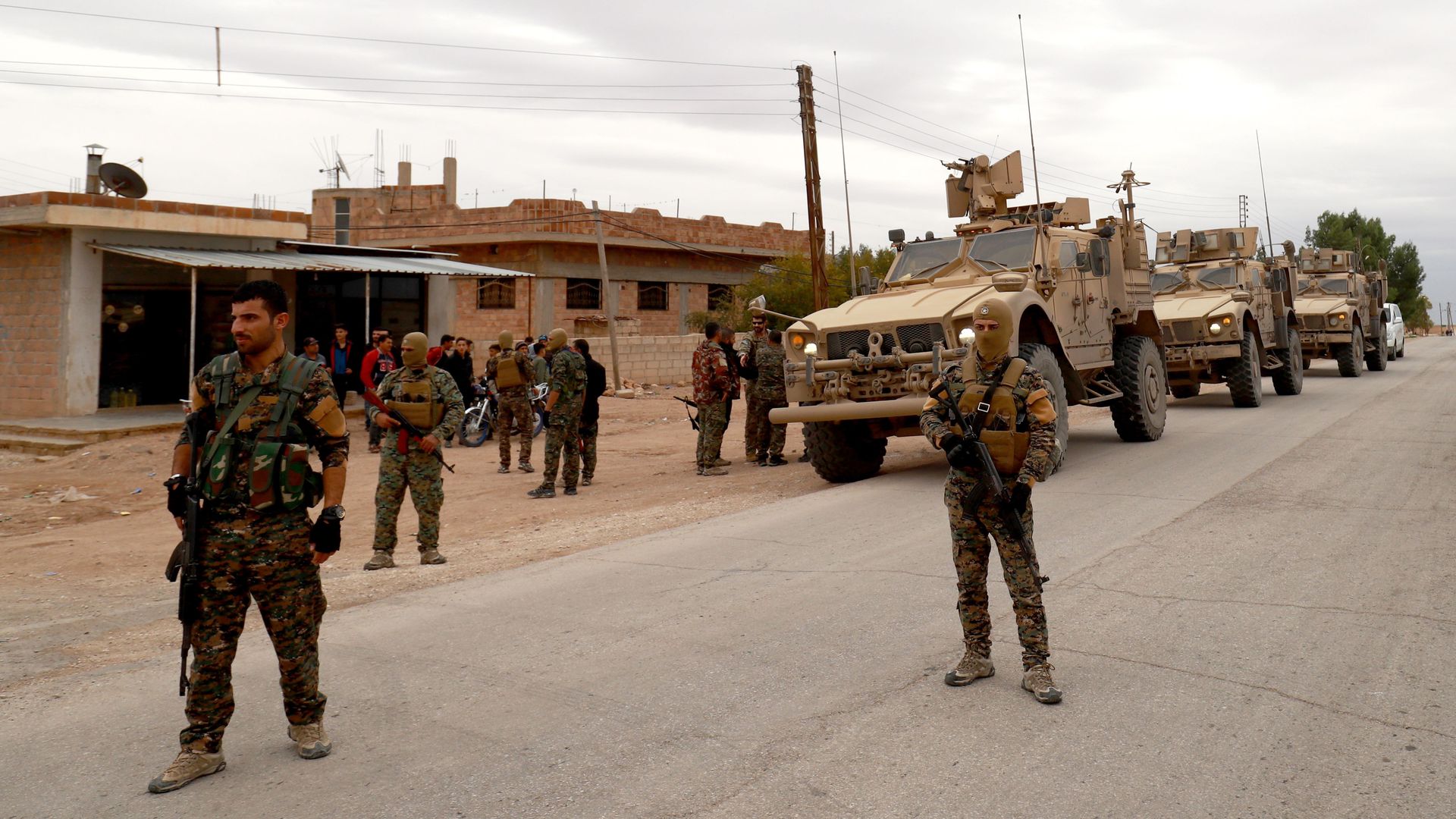 soldiers on foot patrolling a town, with tanks in the background