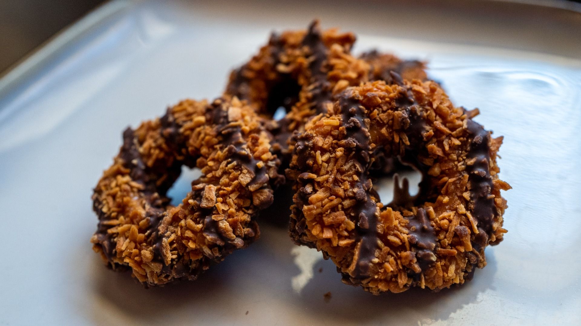 Close up of three Samoa Girl Scout cookies, made with with coconut flakes, caramel and chocolate stripes, featuring a hole in the middle of each. 