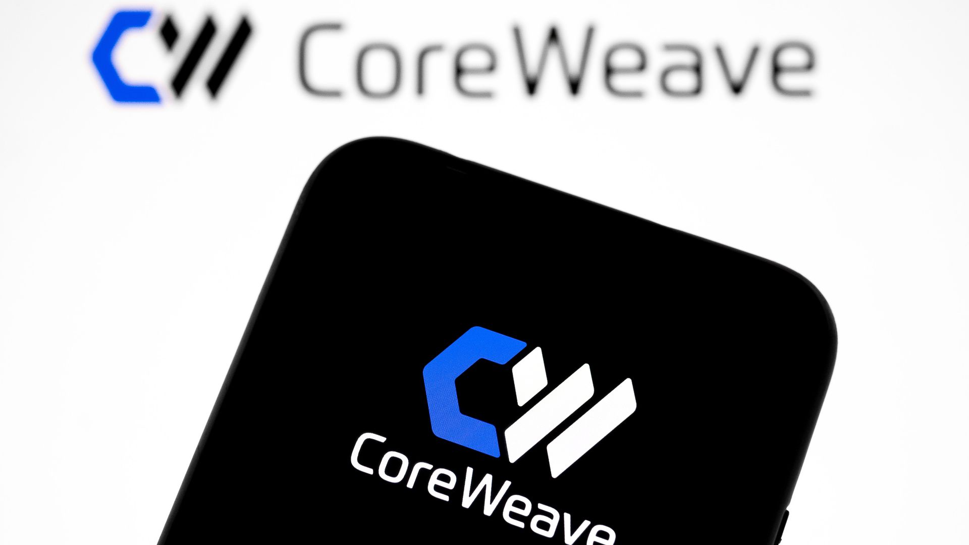 The CoreWeave logo appears on a smartphone screen and as the background on a laptop computer screen in this photo illustration in Athens, Greece, on September 25, 2025. (Photo by Nikolas Kokovlis/NurPhoto via Getty Images)
