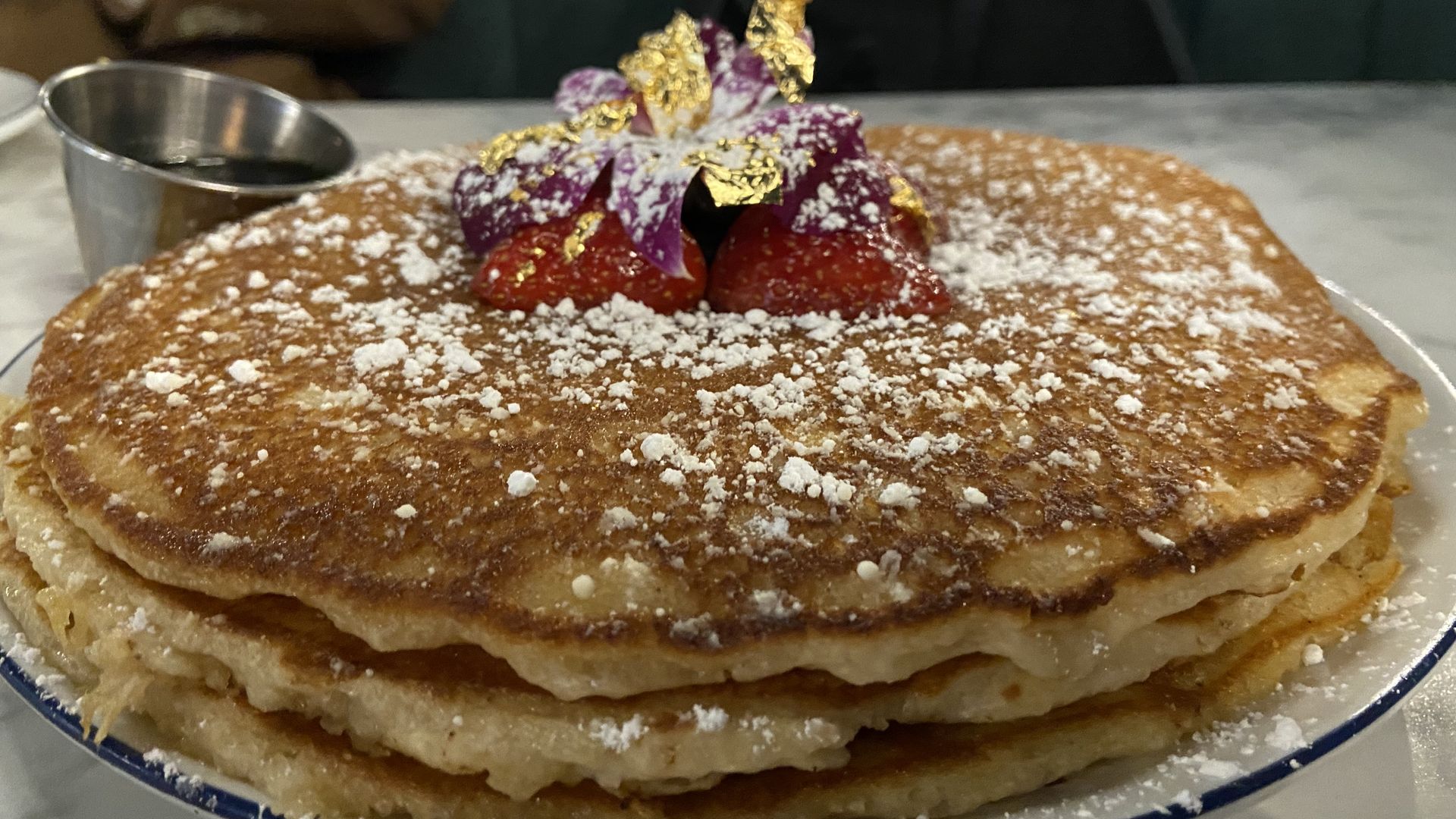 A photo of extra large pancakes, topped with powdered sugar, berries, and edible gold