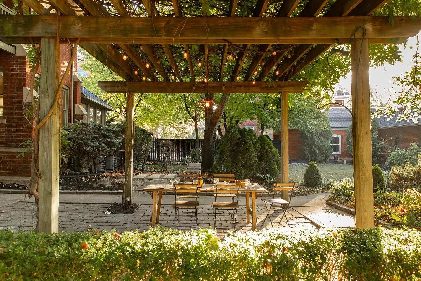 A home's outdoor pergola with dining table in the foreground and trees in the back. 