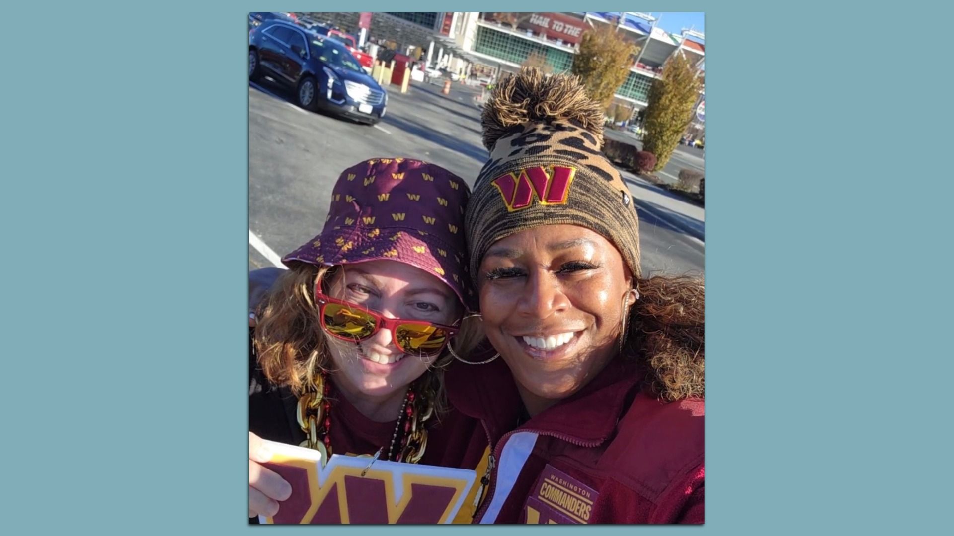 Two women wearing Commanders gear posing in front of the stadium.
