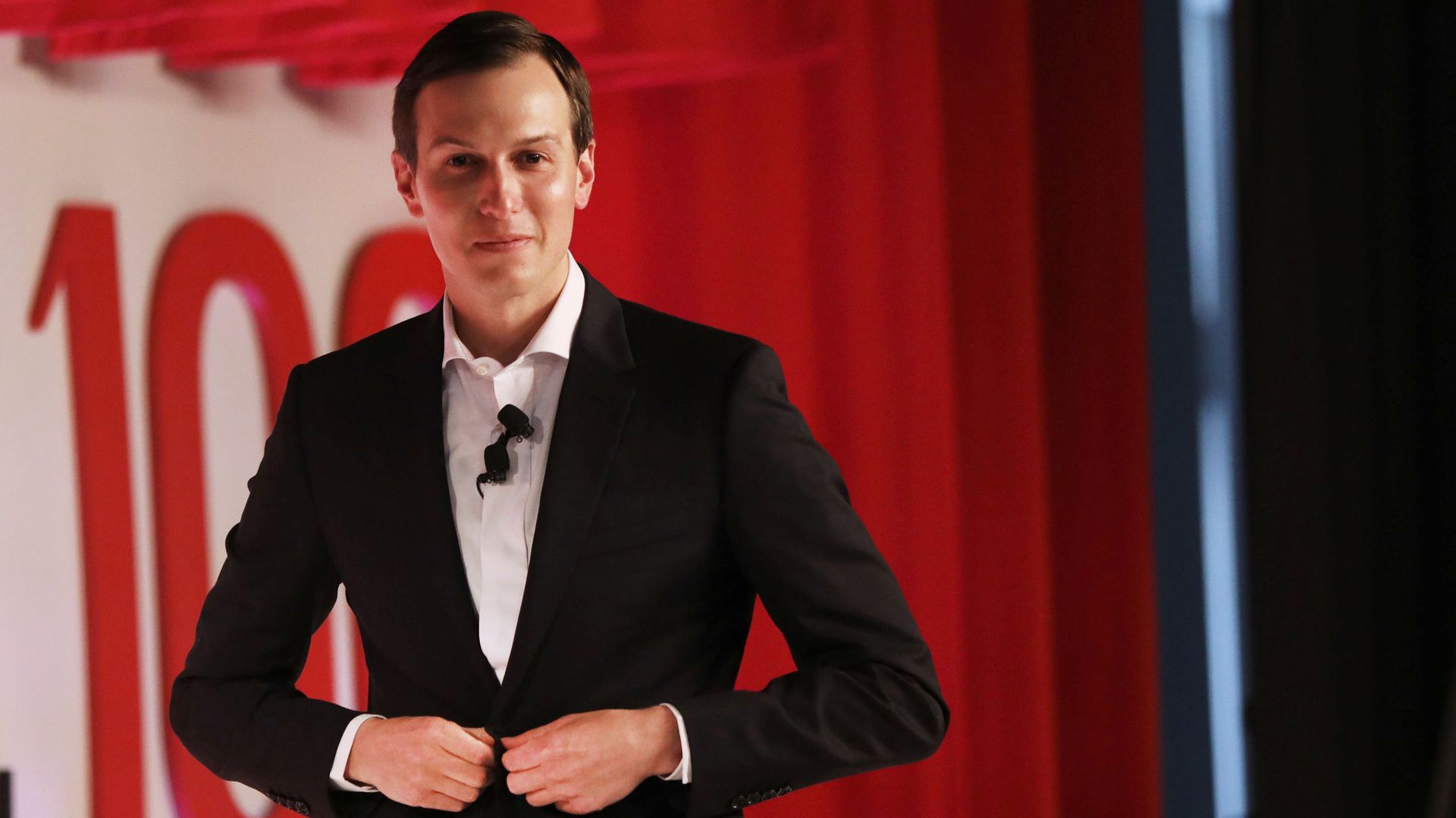 Jared Kushner walking off of a stage at an event while buttoning his blazer. 