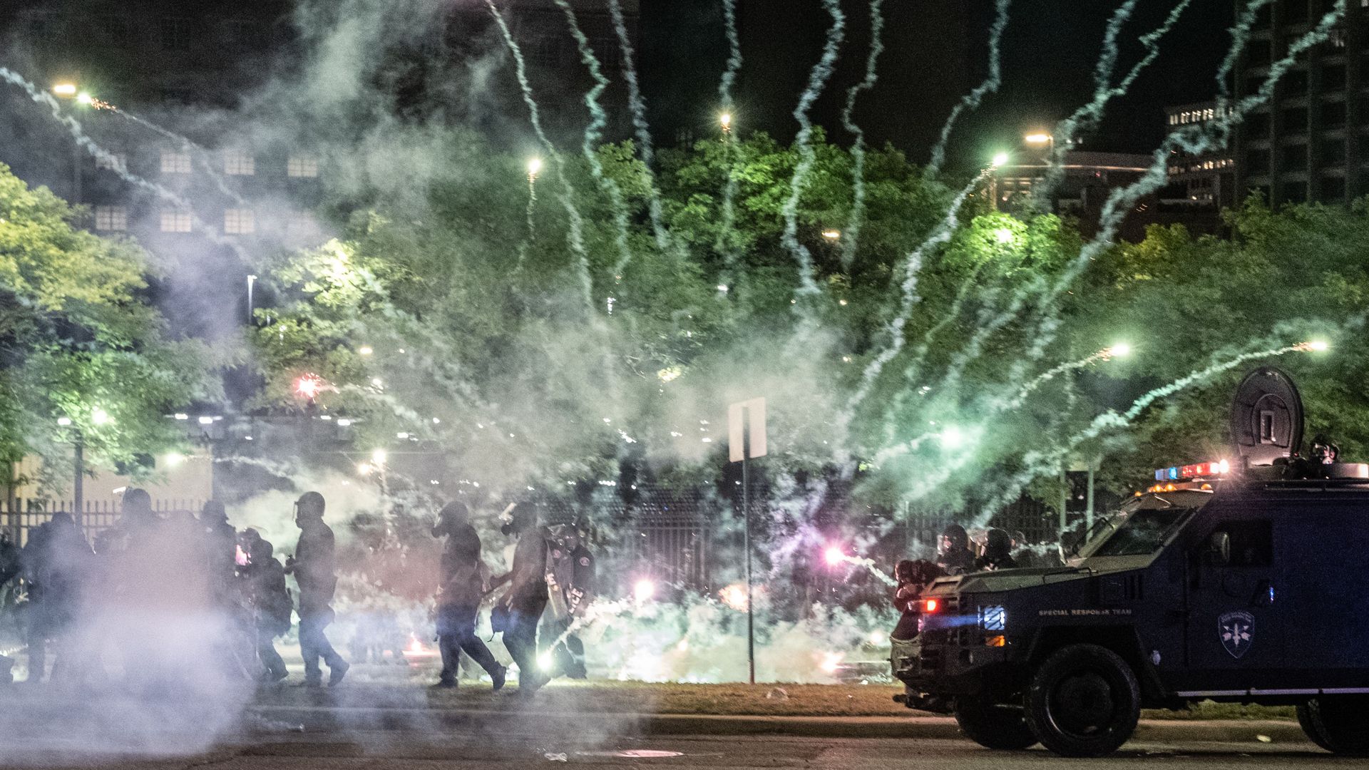 Tear gas canisters go off by protesters and a cop car.