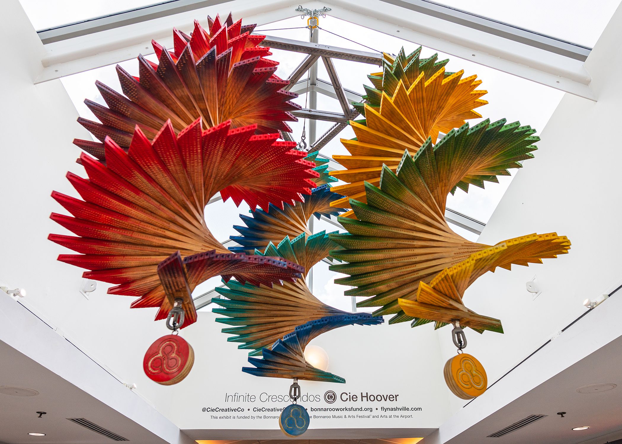 Brightly colored wood sculptures suspended in a skylight.
