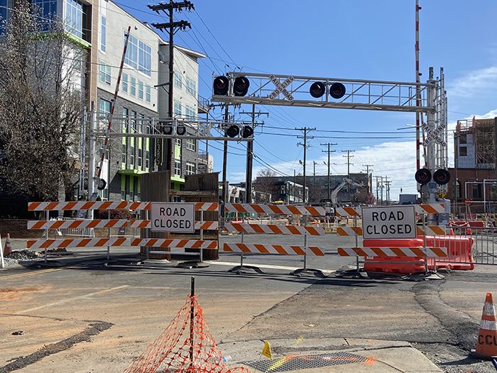 Signs reading "road closed" block off Central Avenue by the train tracks on a sunny day.