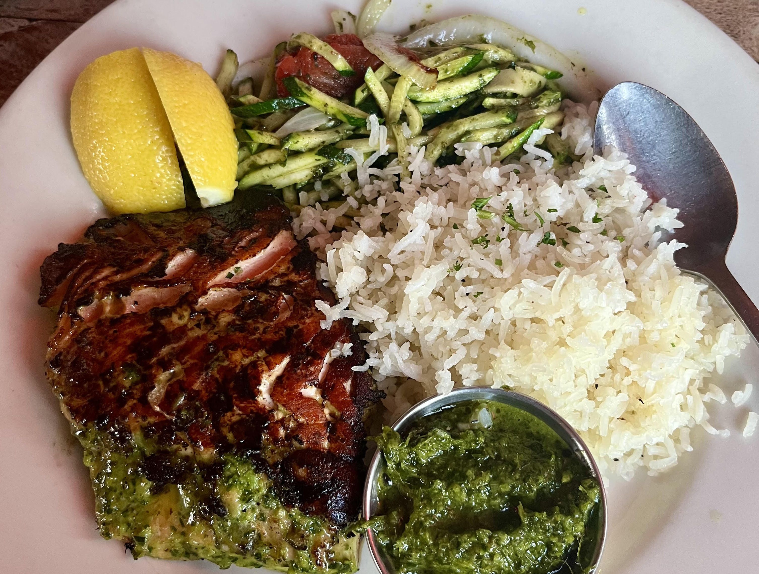 A dish consisting of salmon, a green sauce, rice and zucchini salad.