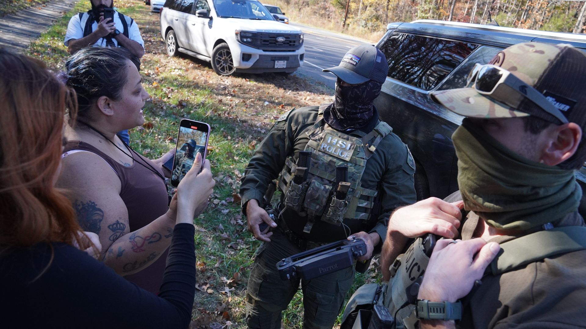 Two people speak to DHS officers while recording on their phones
