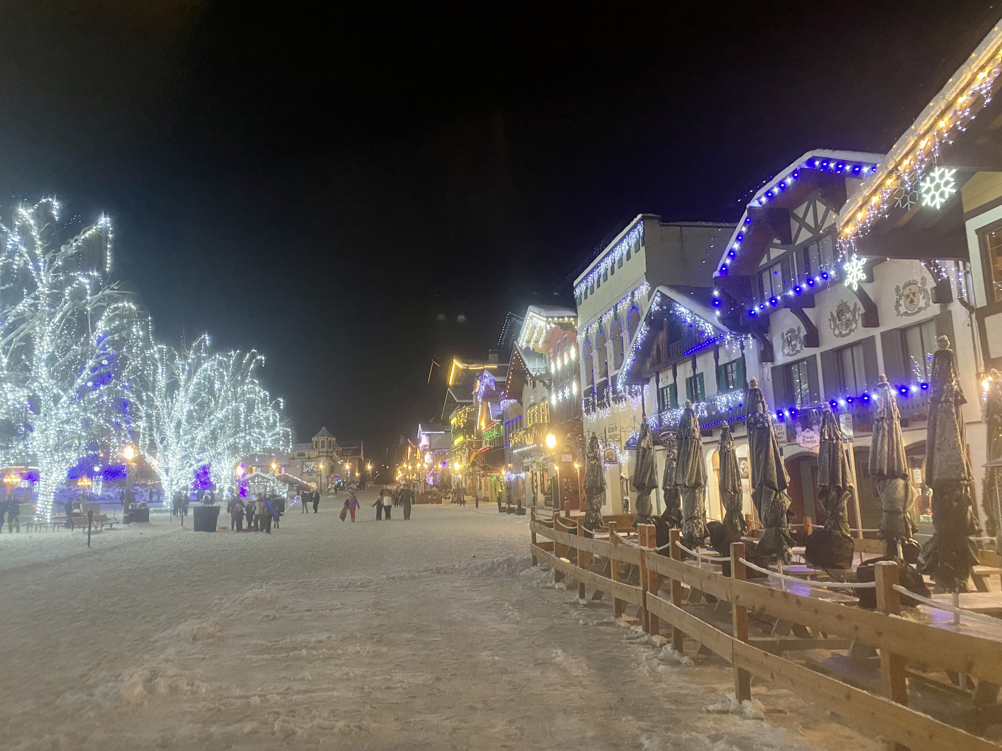 A snowy street with Bavarian-style buildings lining it, all lit with colorful lights.