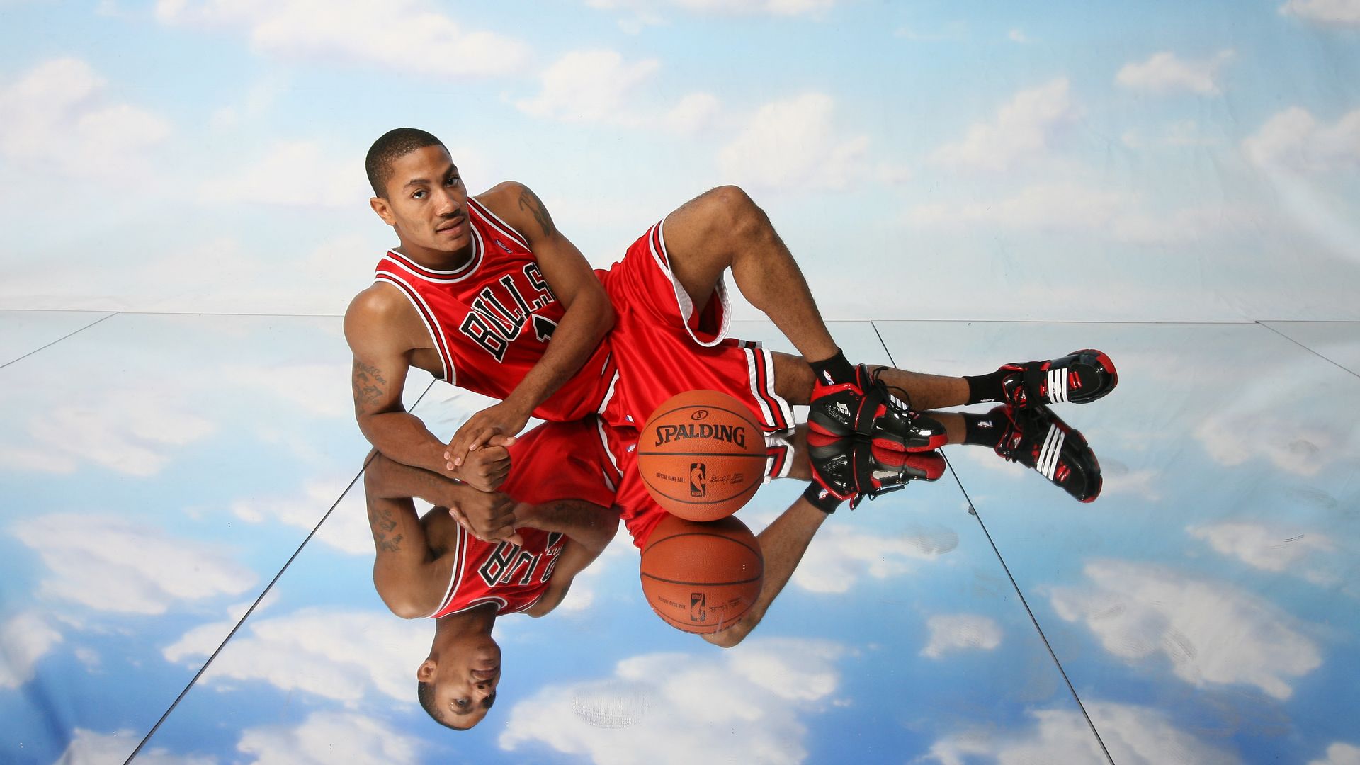 Photo of a basketball player posing for a photo on a mirrored floor that looks like the sky. 