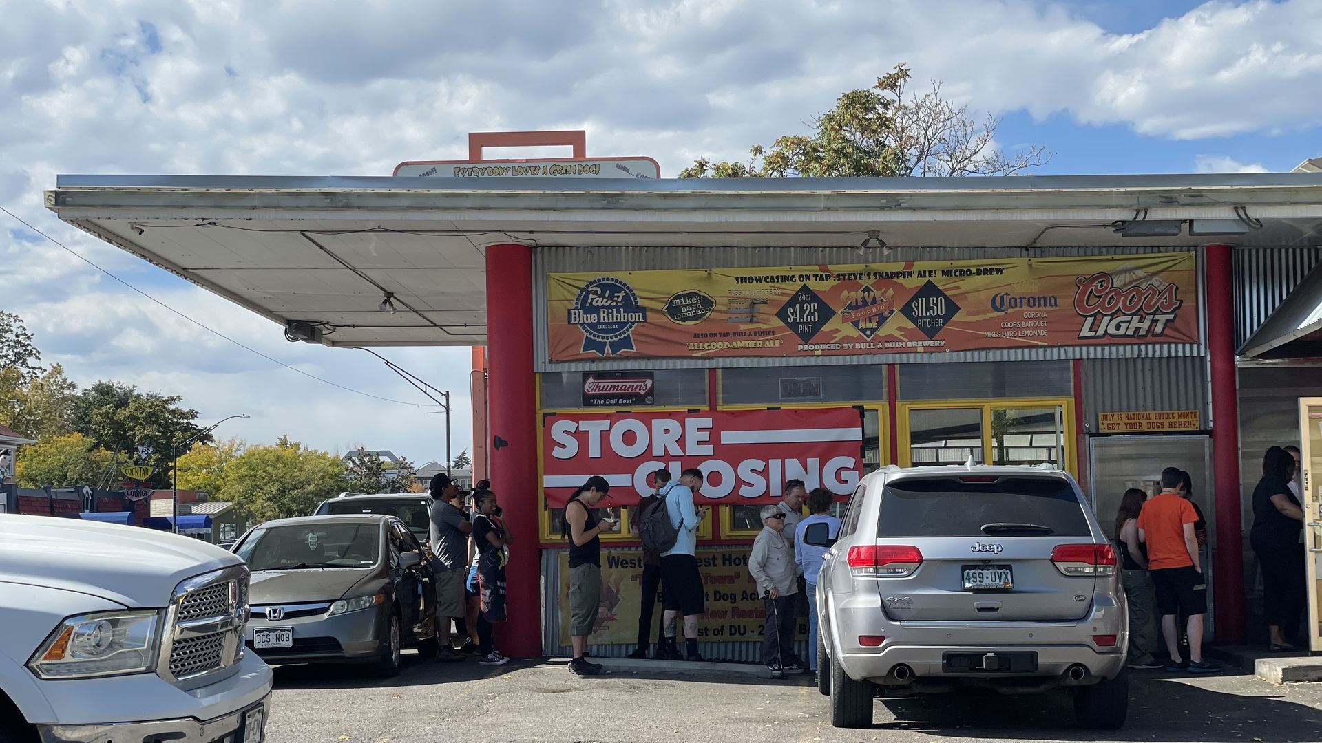 People wait in a line outside a large establishment with the words STORE CLOSING. 