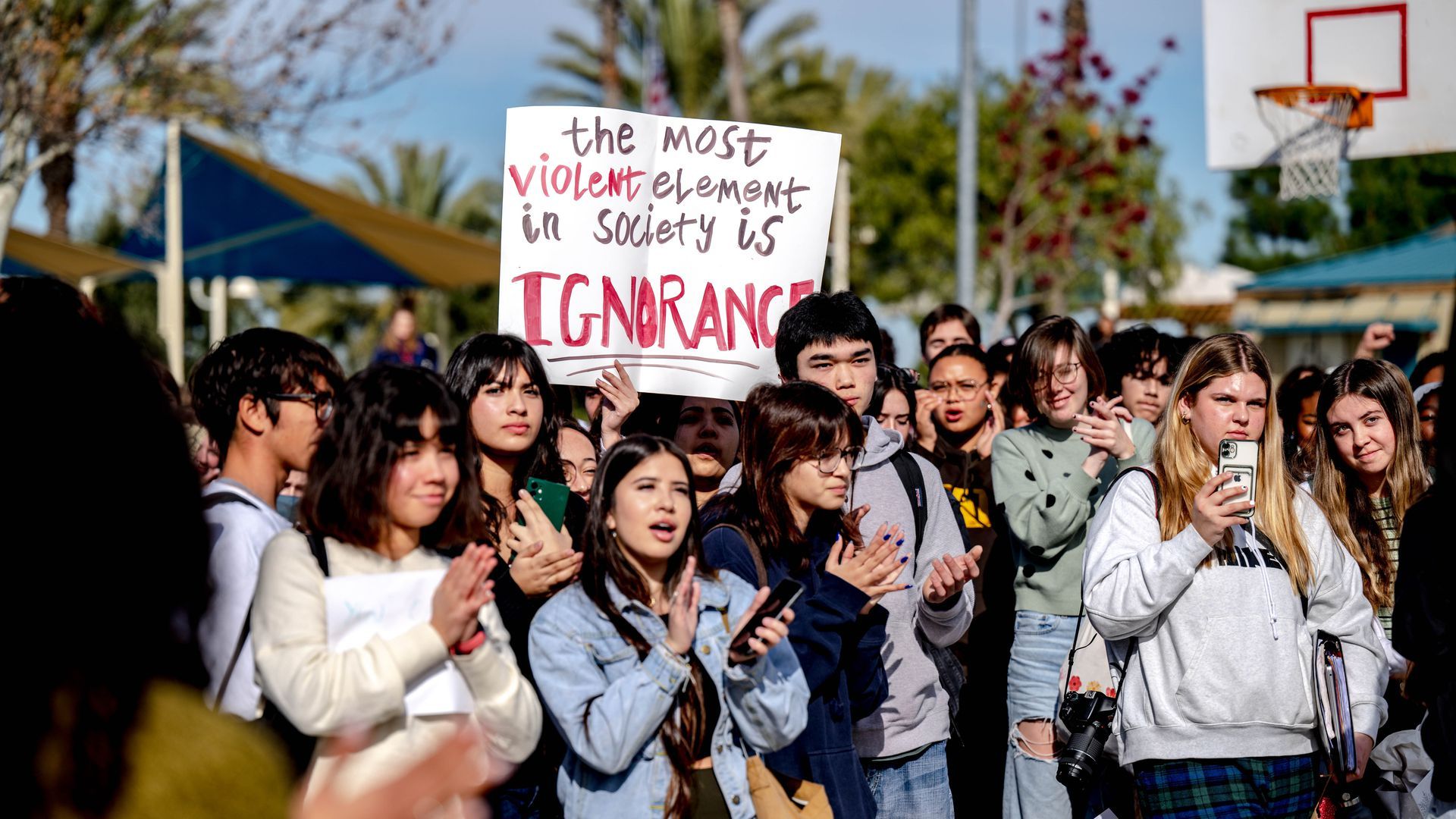 dozens of student protesters stand in california holding a posterboard that reads "the most violent element in society is ignorance"