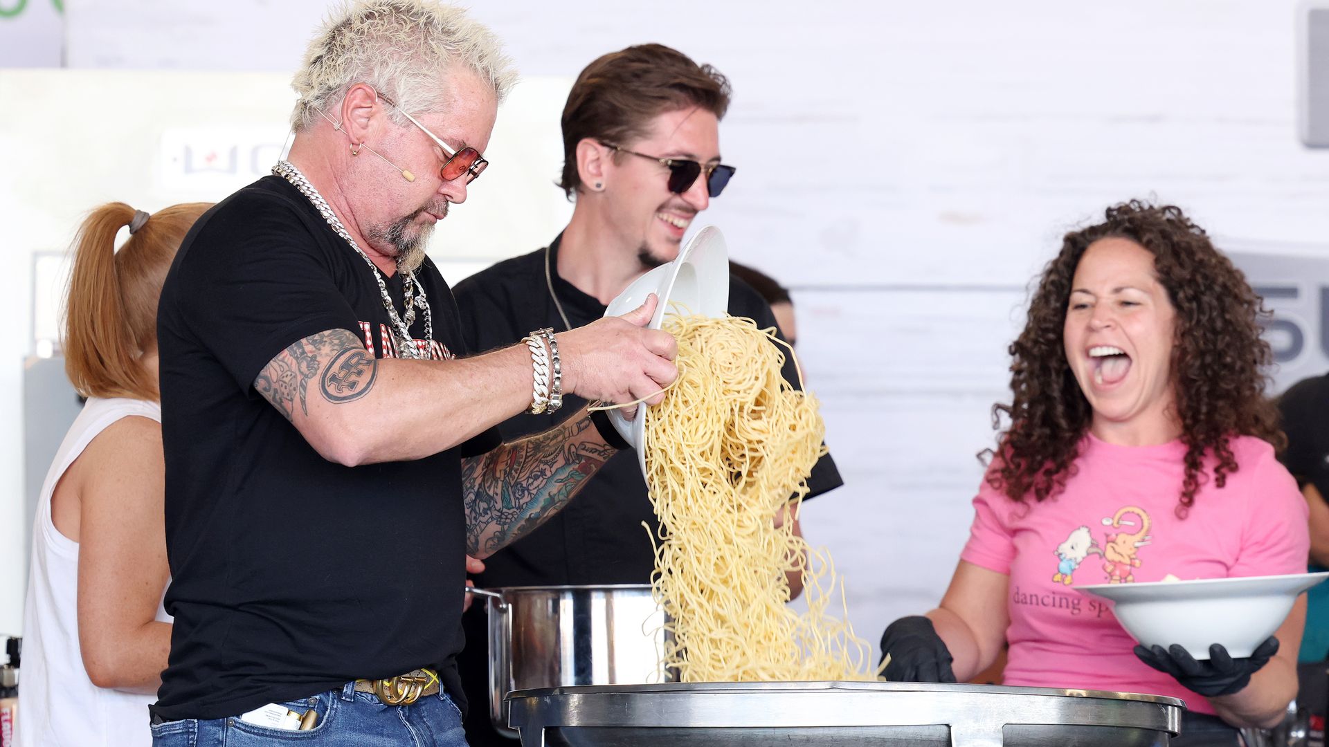 Three people smiling and a big bowl of pasta.