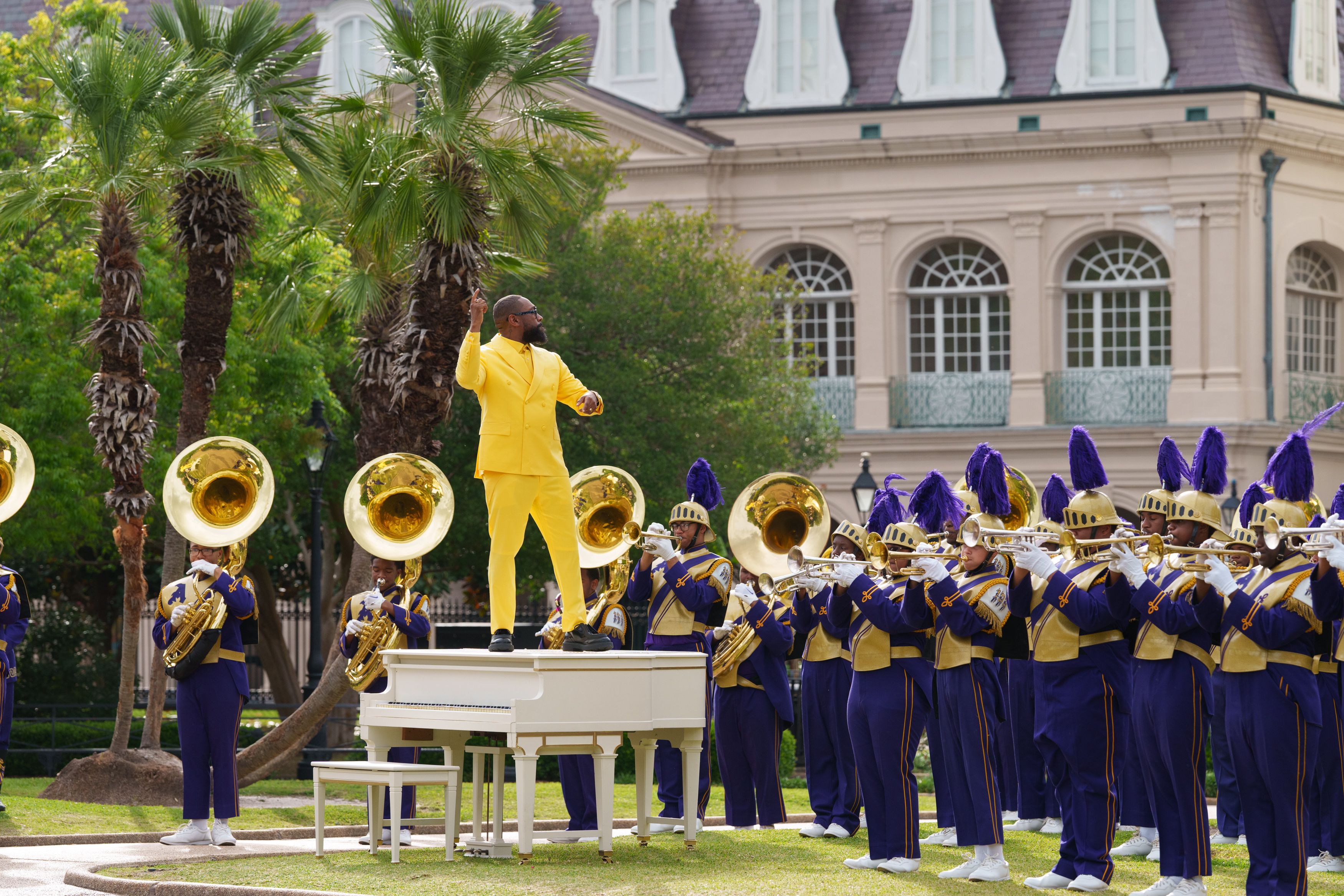 Photo shows PJ Morton standing on a white piano with St. Aug's Marching 100 around him.