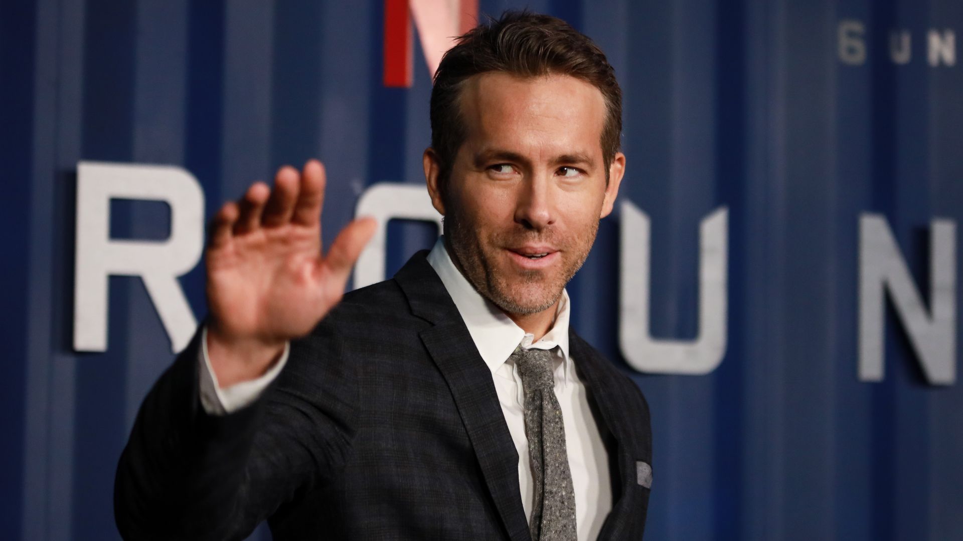 Ryan Reynolds waving at a red carpet event.