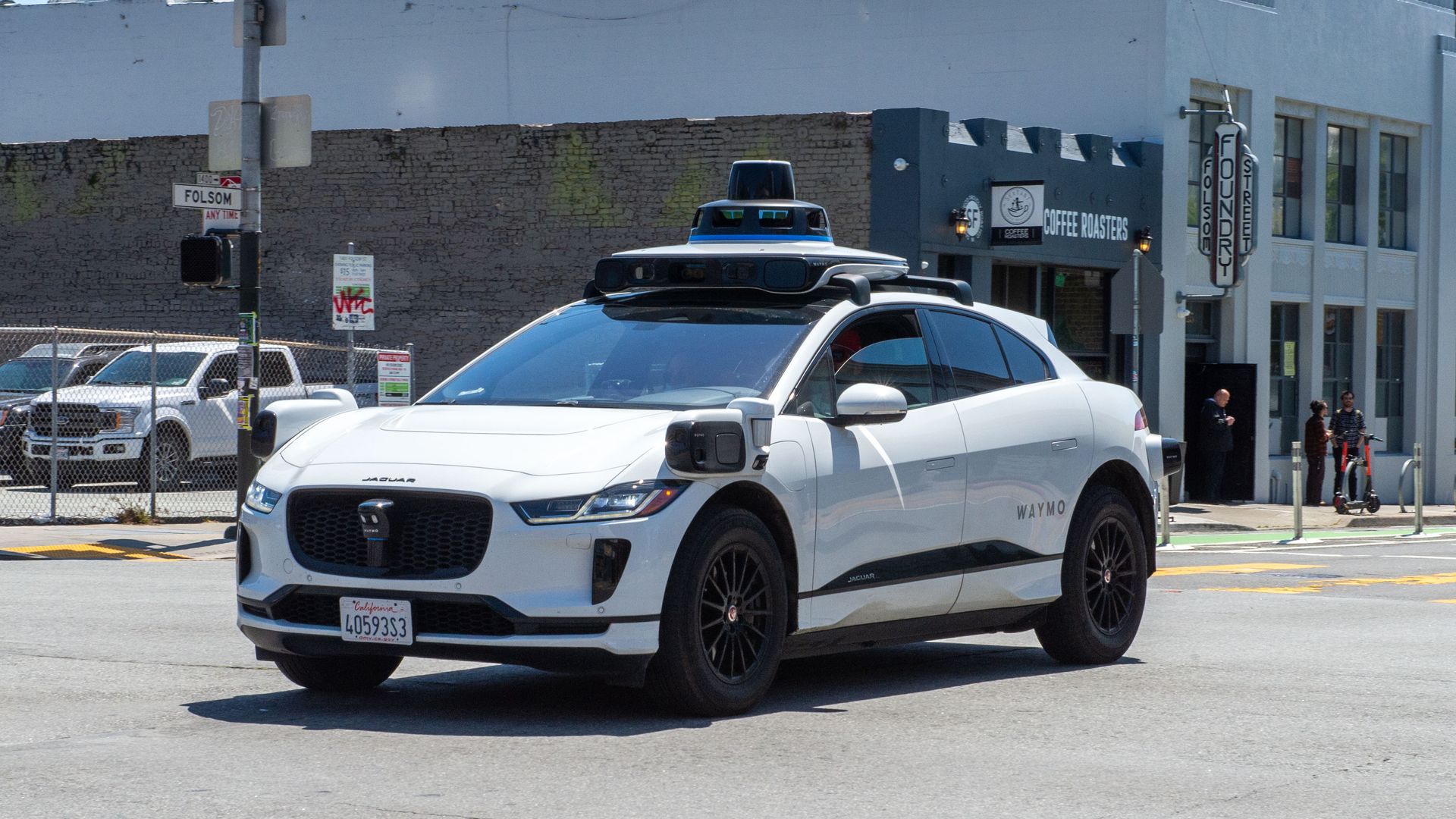 A white self-driving car from Waymo, outfitted with sensors, drives on Folsom street 