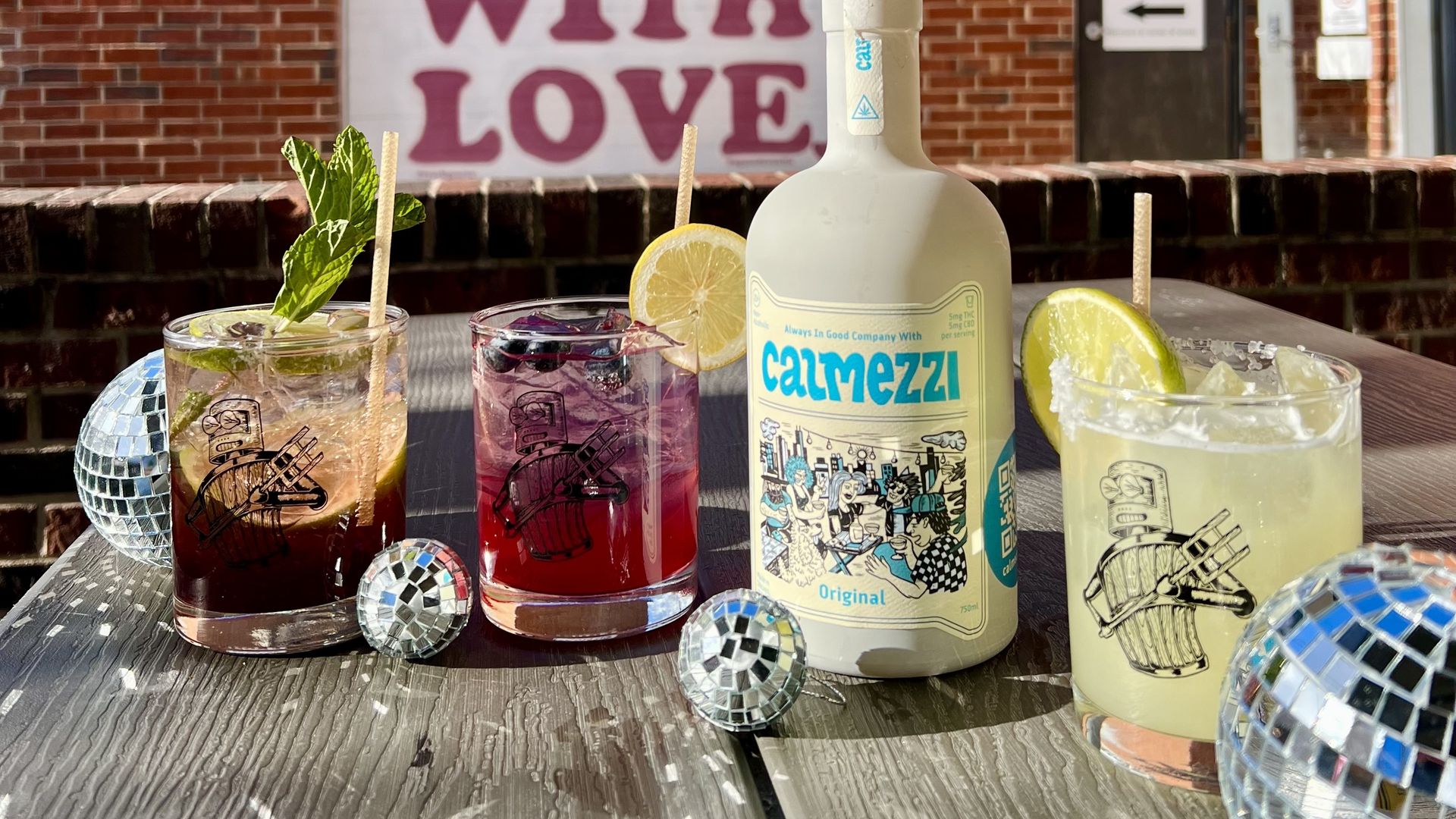 different drinks sit outside on a picnic table next to small disco balls
