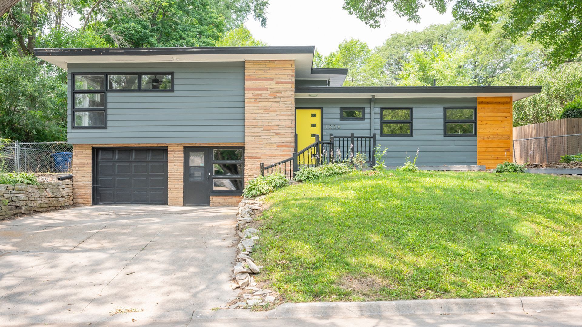 A mid-modern split-level home for sale is Des Moines with a yellow front door.