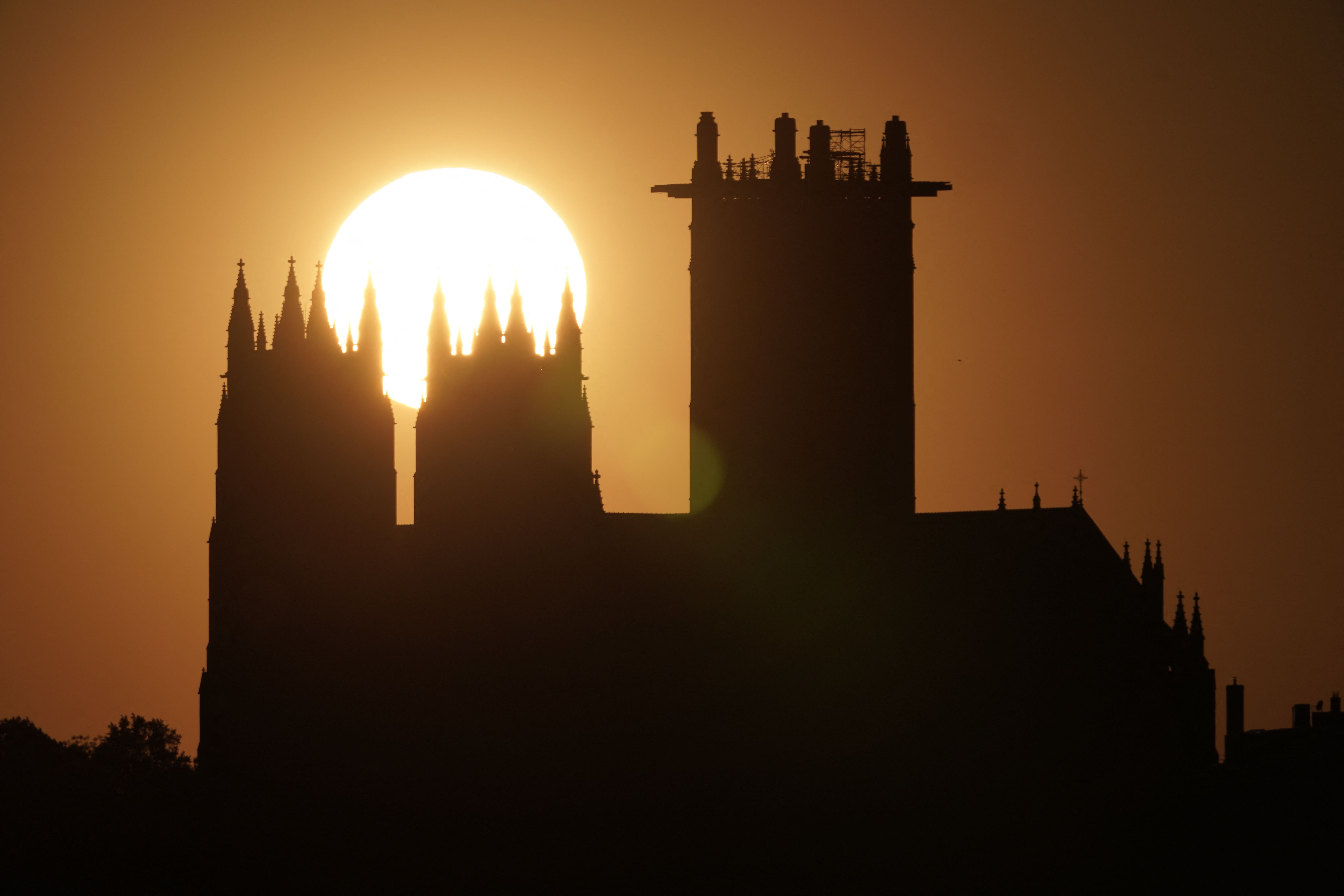 Silhouette of the National Cathedral with Gothic spires on the left and a tall rectangular tower on the right, set against a large orange sunset.