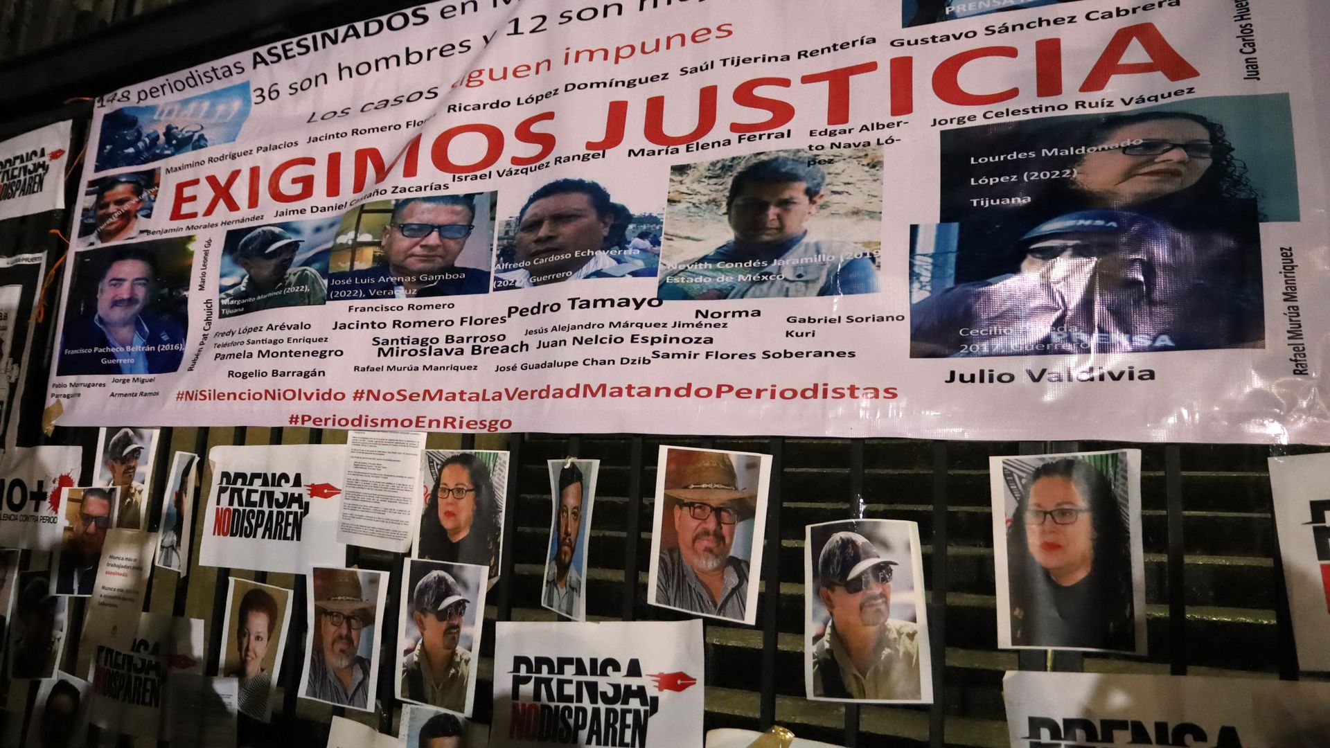 A wall with photos and names of Mexican journalists who have been murdered. There is also a sign that says "we demand justice" in Spanish. 
