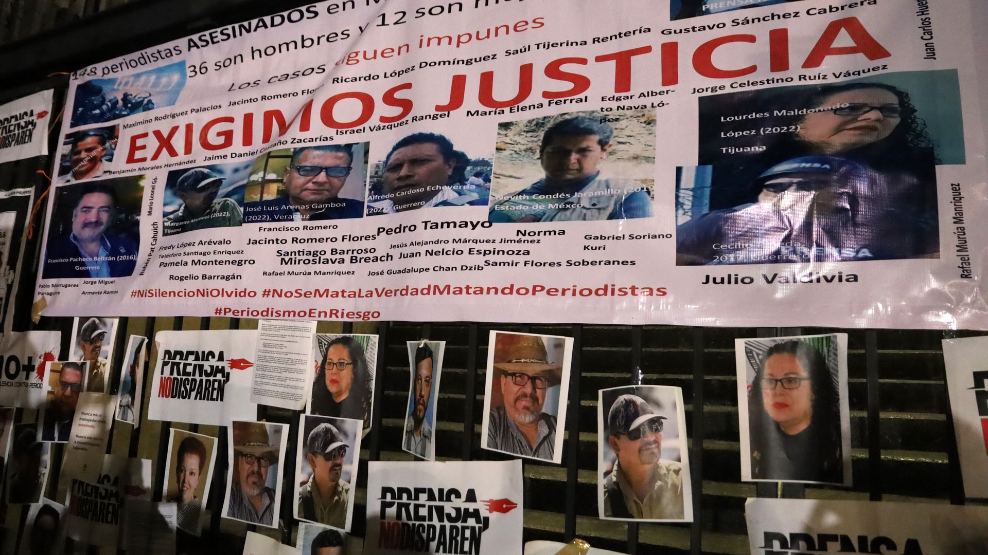 A wall with photos and names of Mexican journalists who have been murdered. There is also a sign that says "we demand justice" in Spanish.