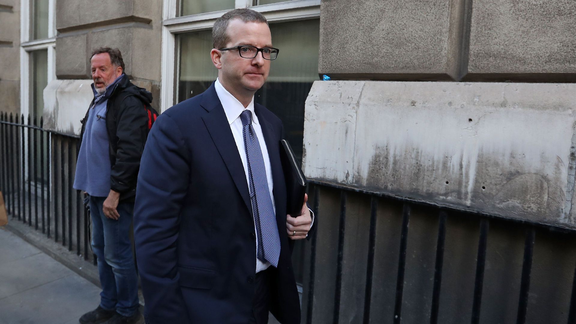 Mike Schroepfer walks, wearing a suit, with a man standing behind him