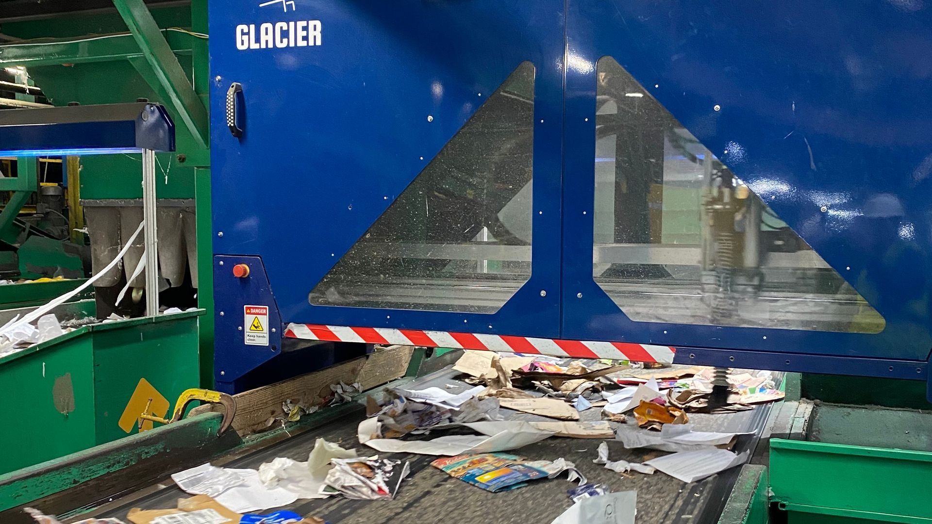 Glacier's Ai-powered robot sorting trash on a moving conveyor belt inside a recycling facility.