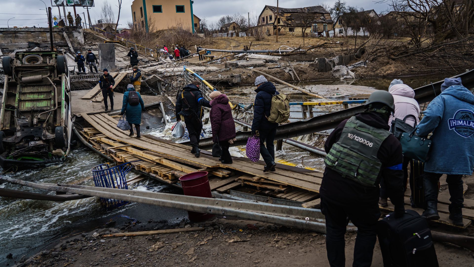 Ukrainian soldiers aid civilians cross a makeshift walkway over a destroyed bridge to evacuate out of Irpin, Ukraine, Sunday, March 13
