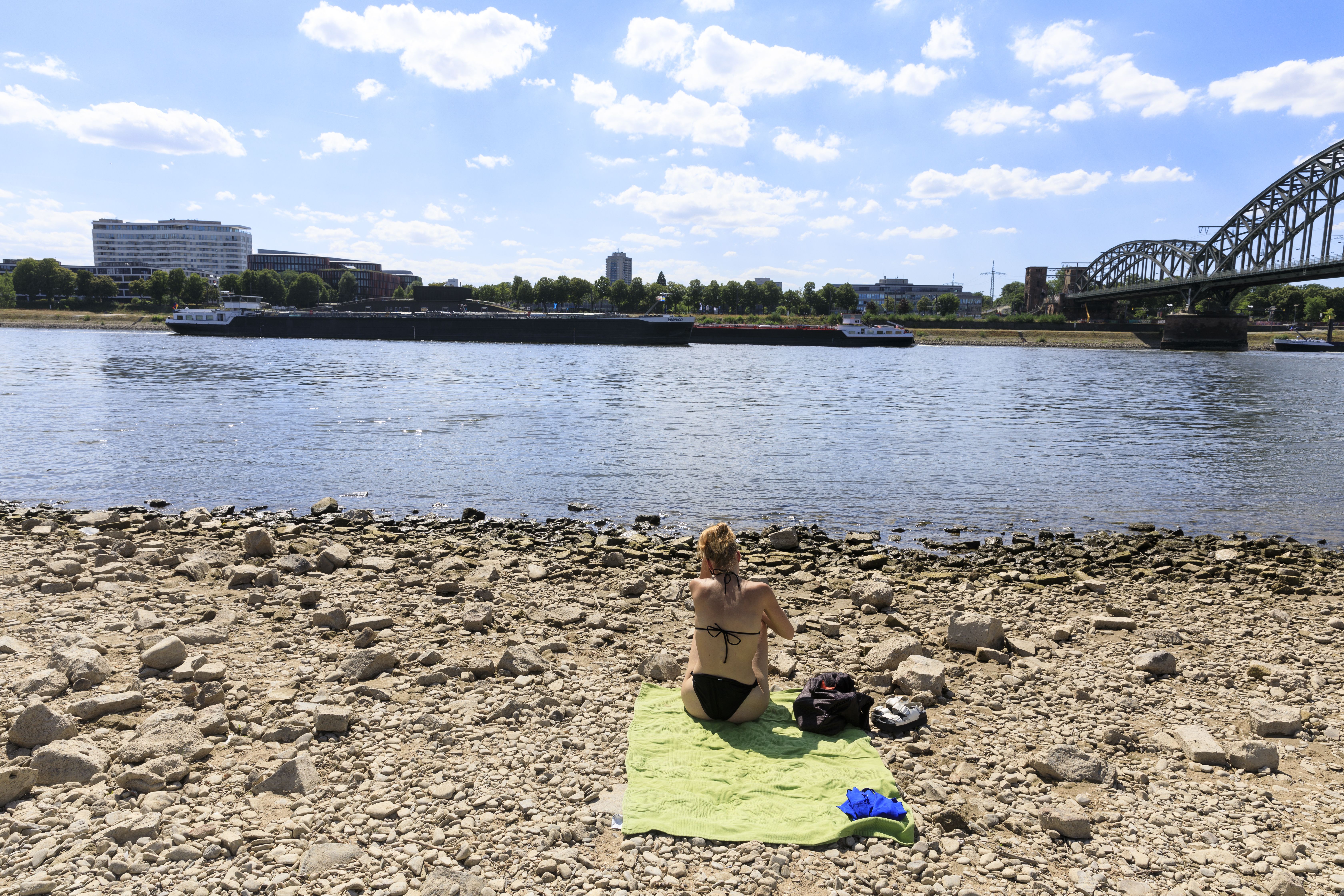Люди сидят на высохшем берегу Рейна 3 августа 2022 года в Кельне, Германия. 
