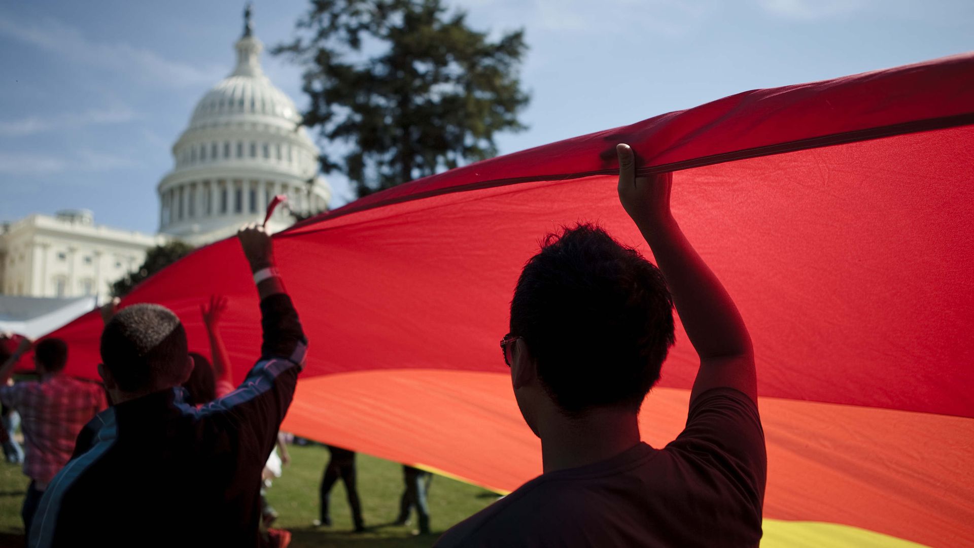 Two men hold a rainbow flag with the US Capitol in the background.