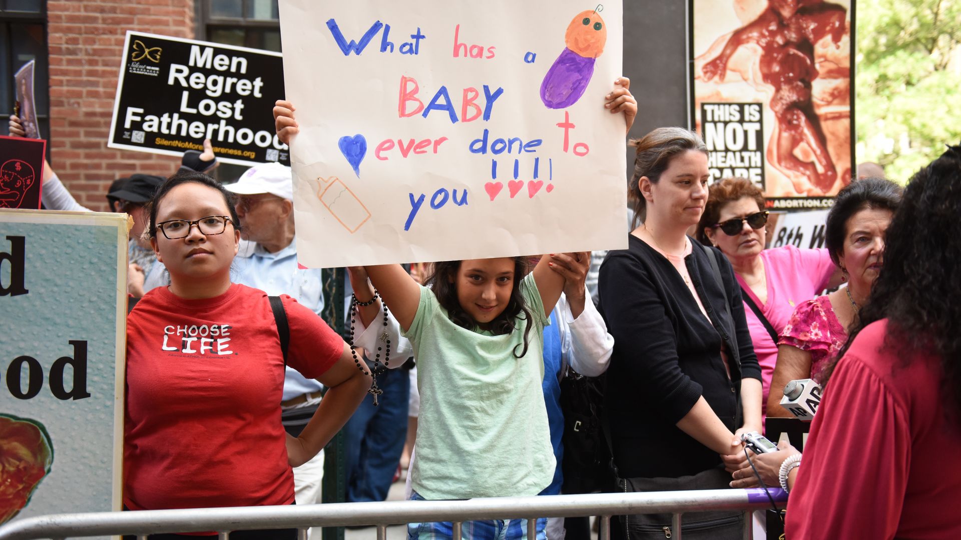 Girl holds up hand-lettered sign in front of Planned Parenthood.