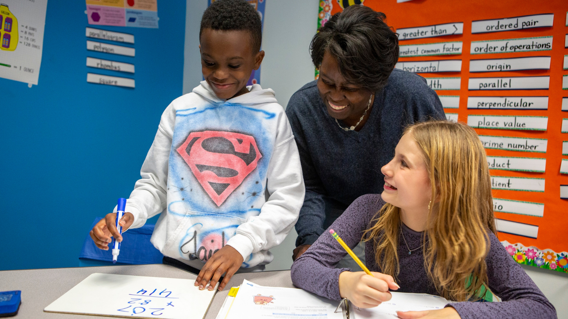 Two children collaborate with a teacher on a project, showcasing teamwork and learning in a classroom setting.