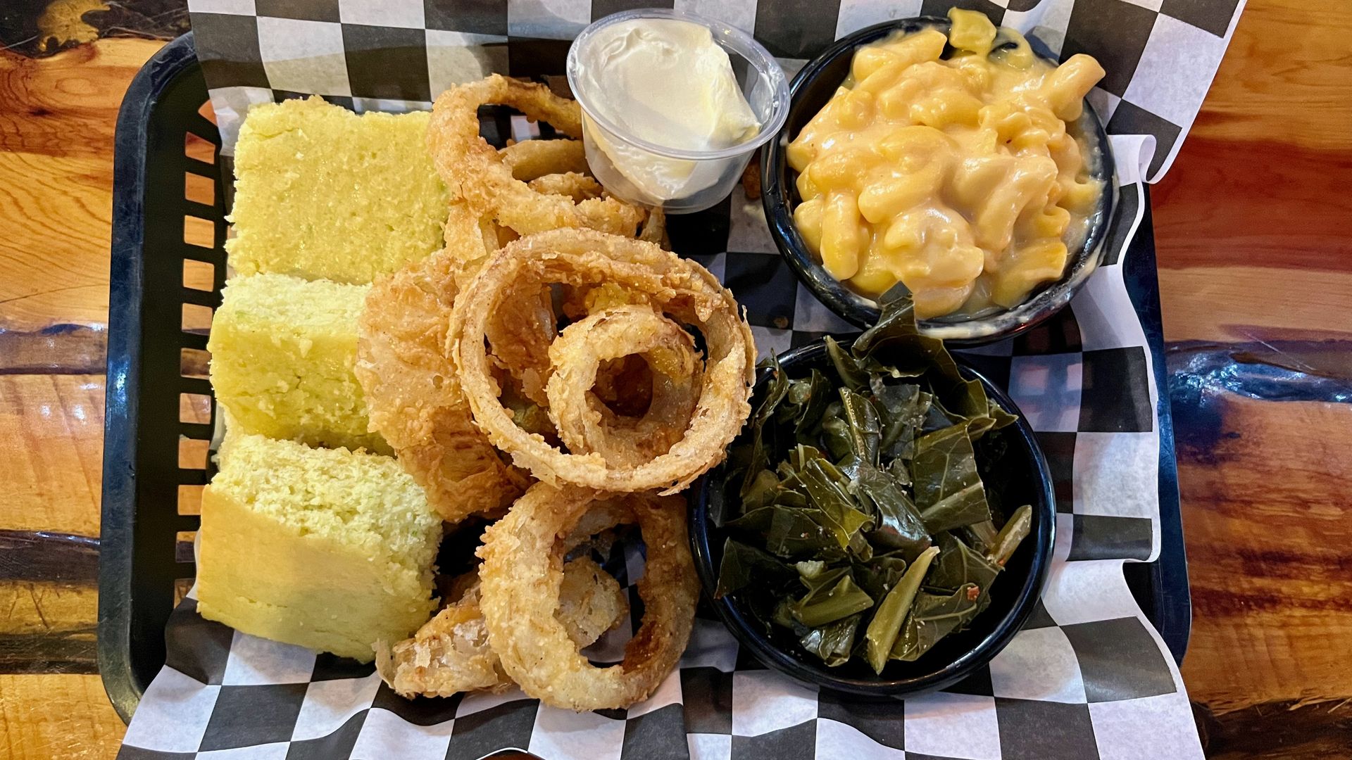 A basket with corn bread, onion rings, mac and cheese and greens