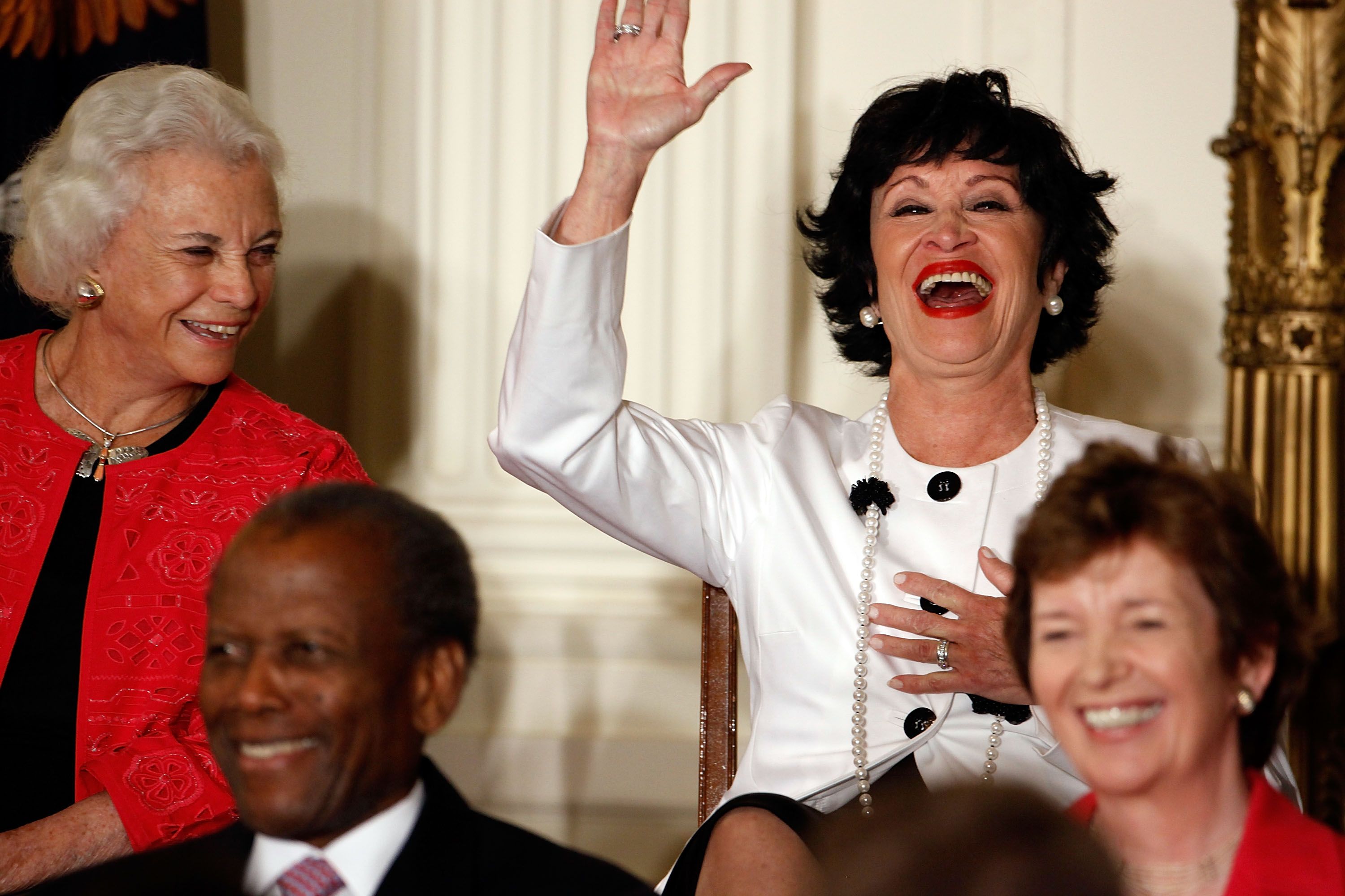 On the left, former Supreme Court Justice Sandra Day O'Connor looks and smiles at Chita Rivera, who is waving at a crowd and laughing