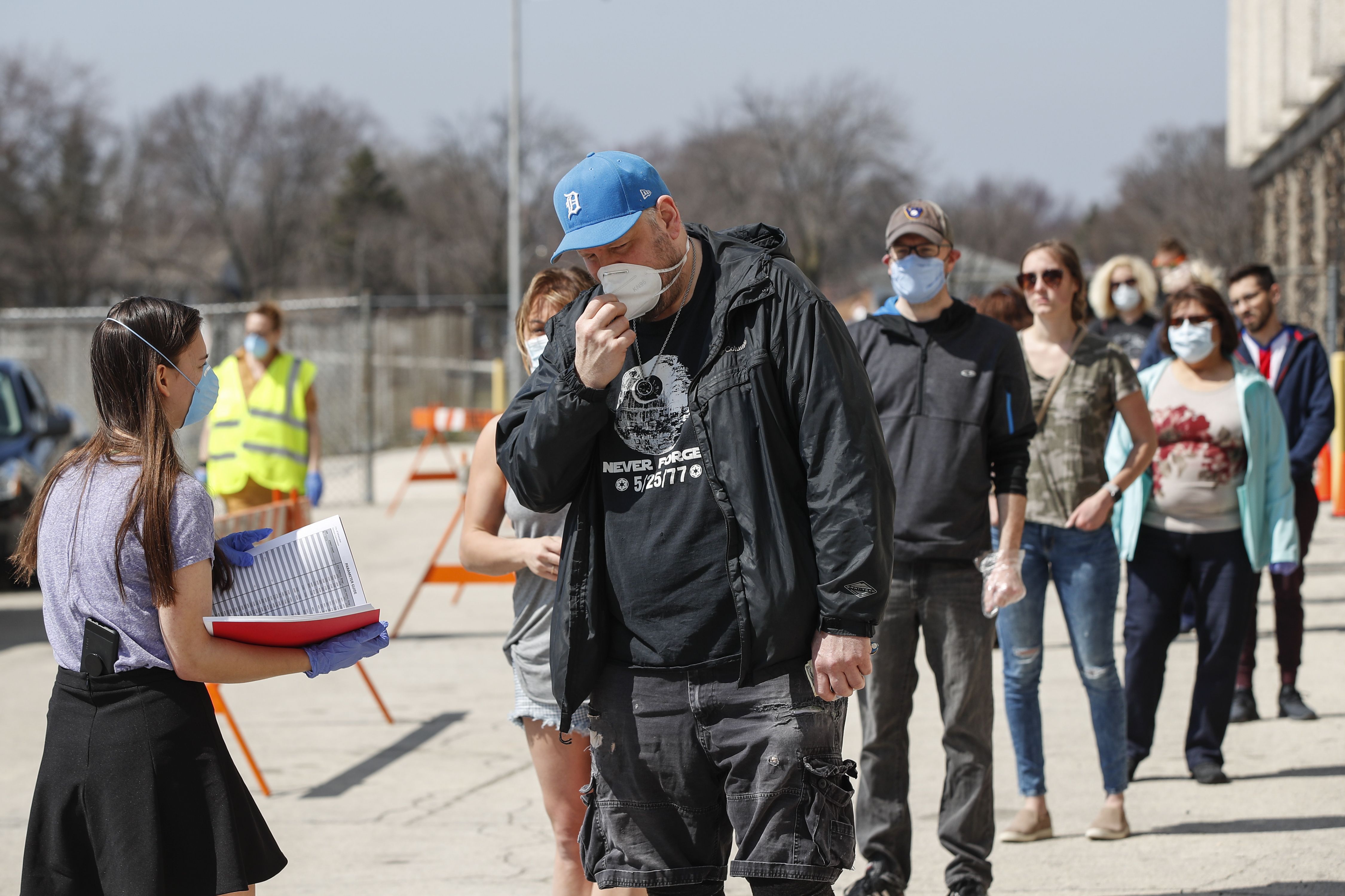 In this image, a line of people wearing face masks stand outside