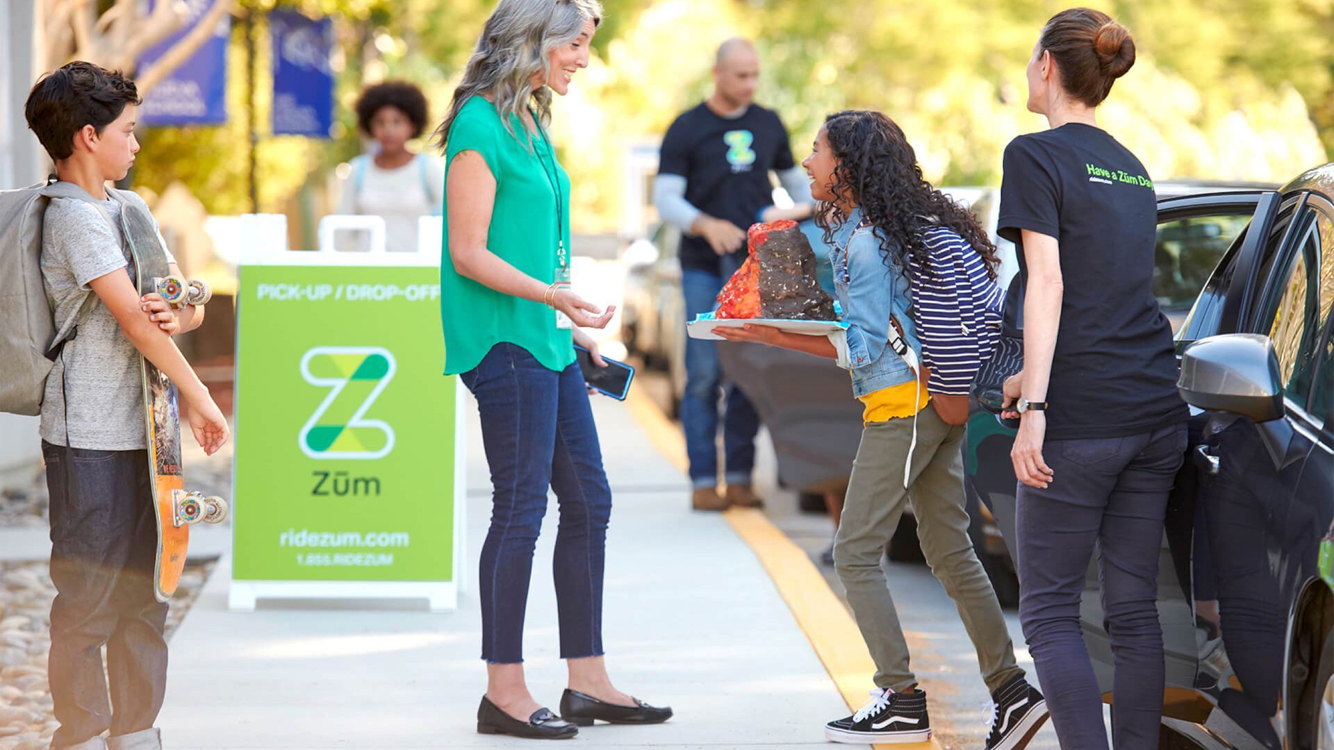 Photo of parent greeting school child on a curb with a Zum sign in background