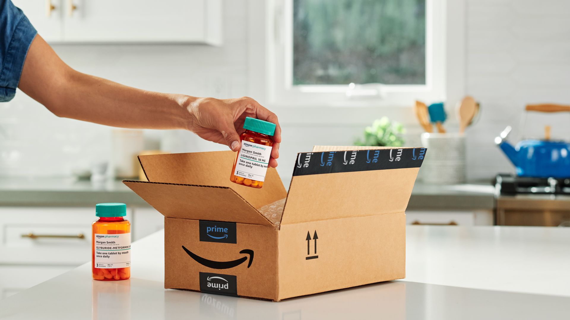 Hand reaching into Amazon box taking out pill bottle with another prescription bottle to left of box