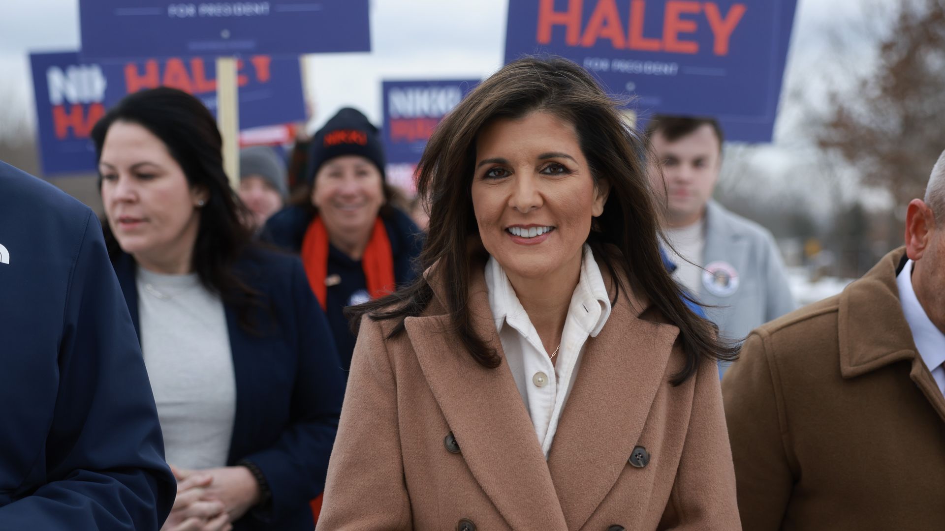 Nikki Haley wearing a blue coat walks with people holding signs in her support 