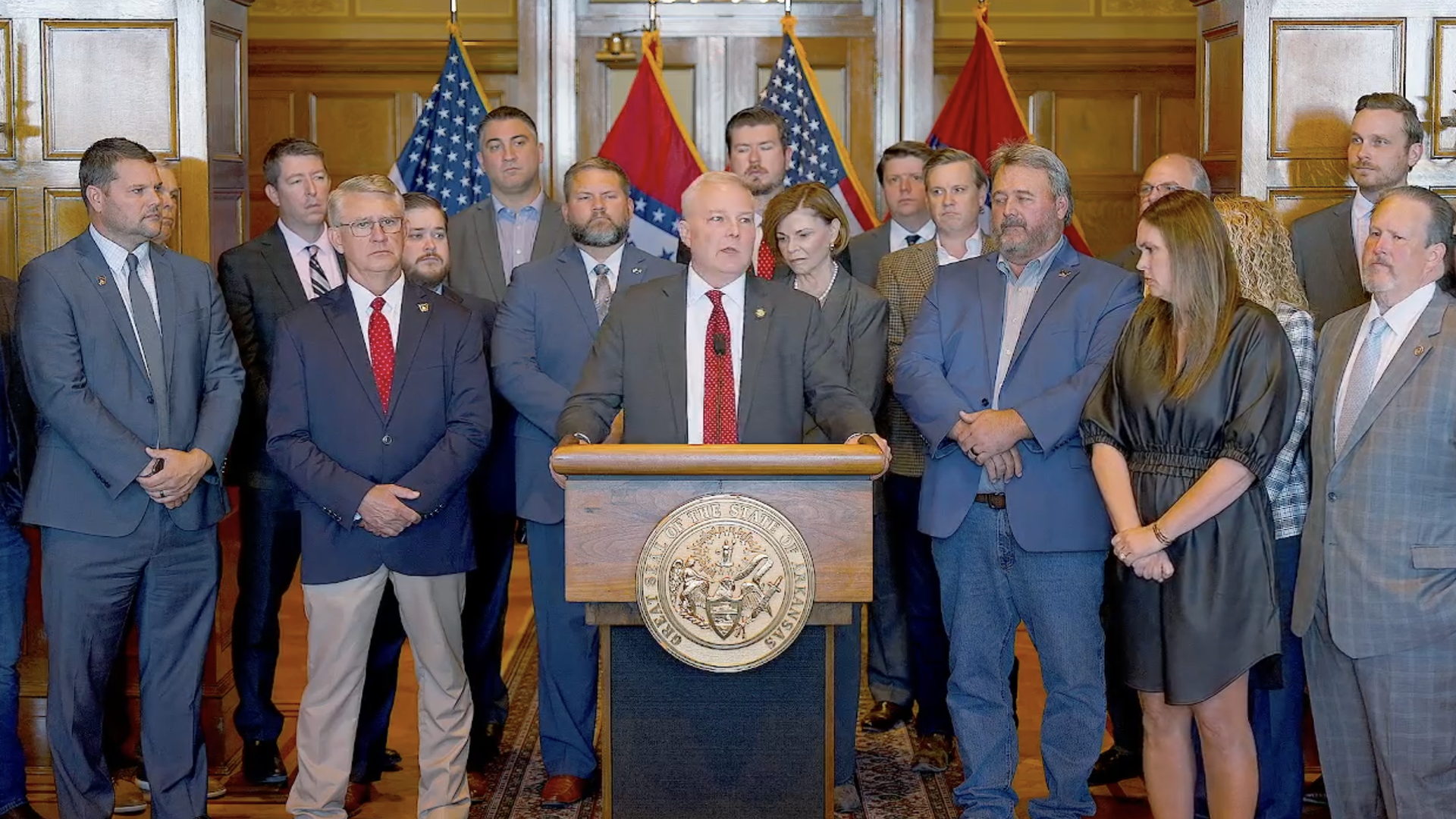 A screenshot of a press conference where Arkansas Attorney General Tim Griffin speaks from the podium, flanked by Gov. Sanders, cabinet members and lawmakers.