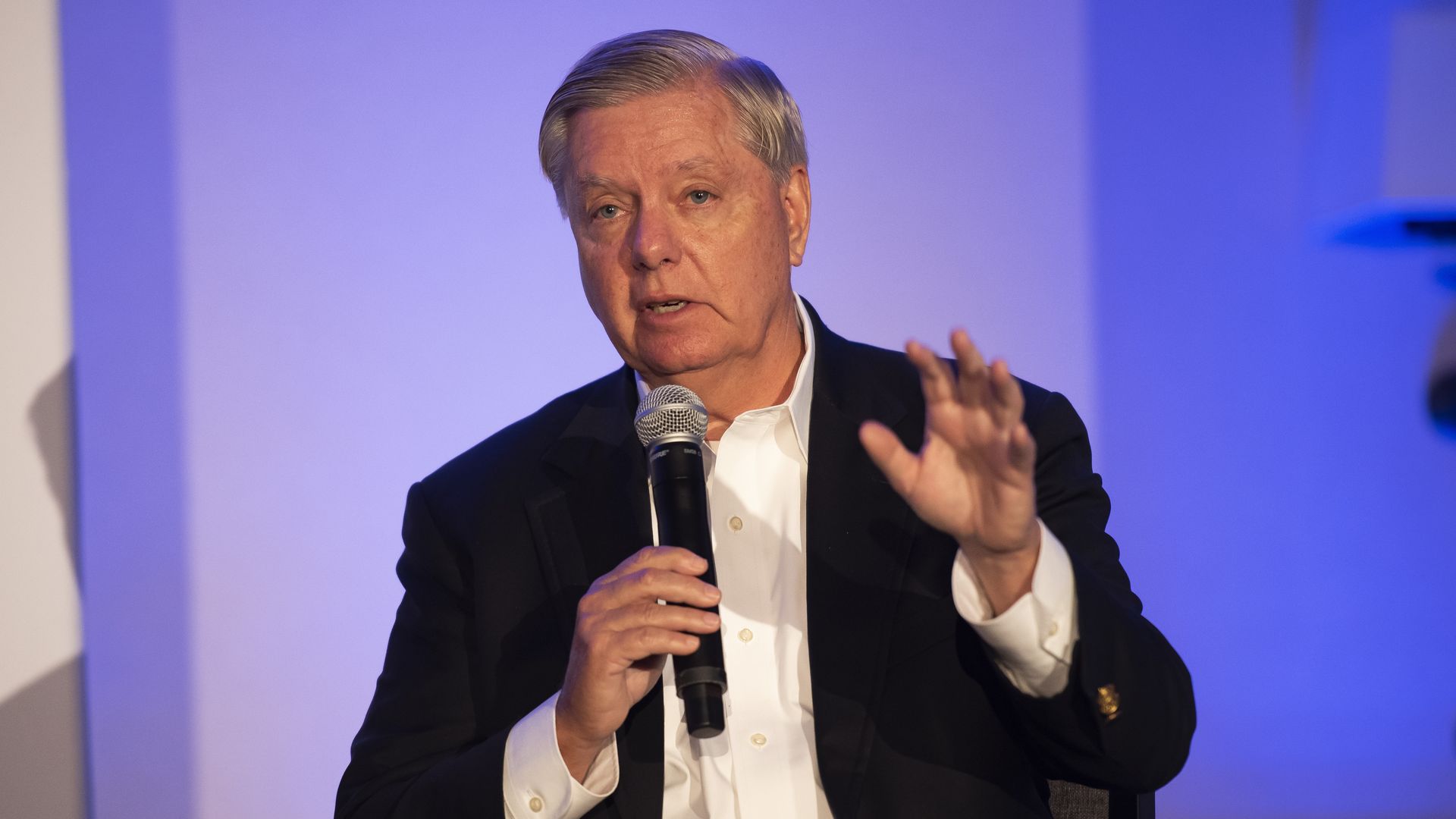 Photo of Lindsey Graham speaking while holding a mic and gesturing with his left hand