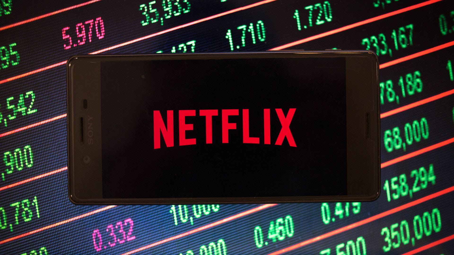 An illustration of the Netflix logo on a phone, set against a screen of numbers from the stock market