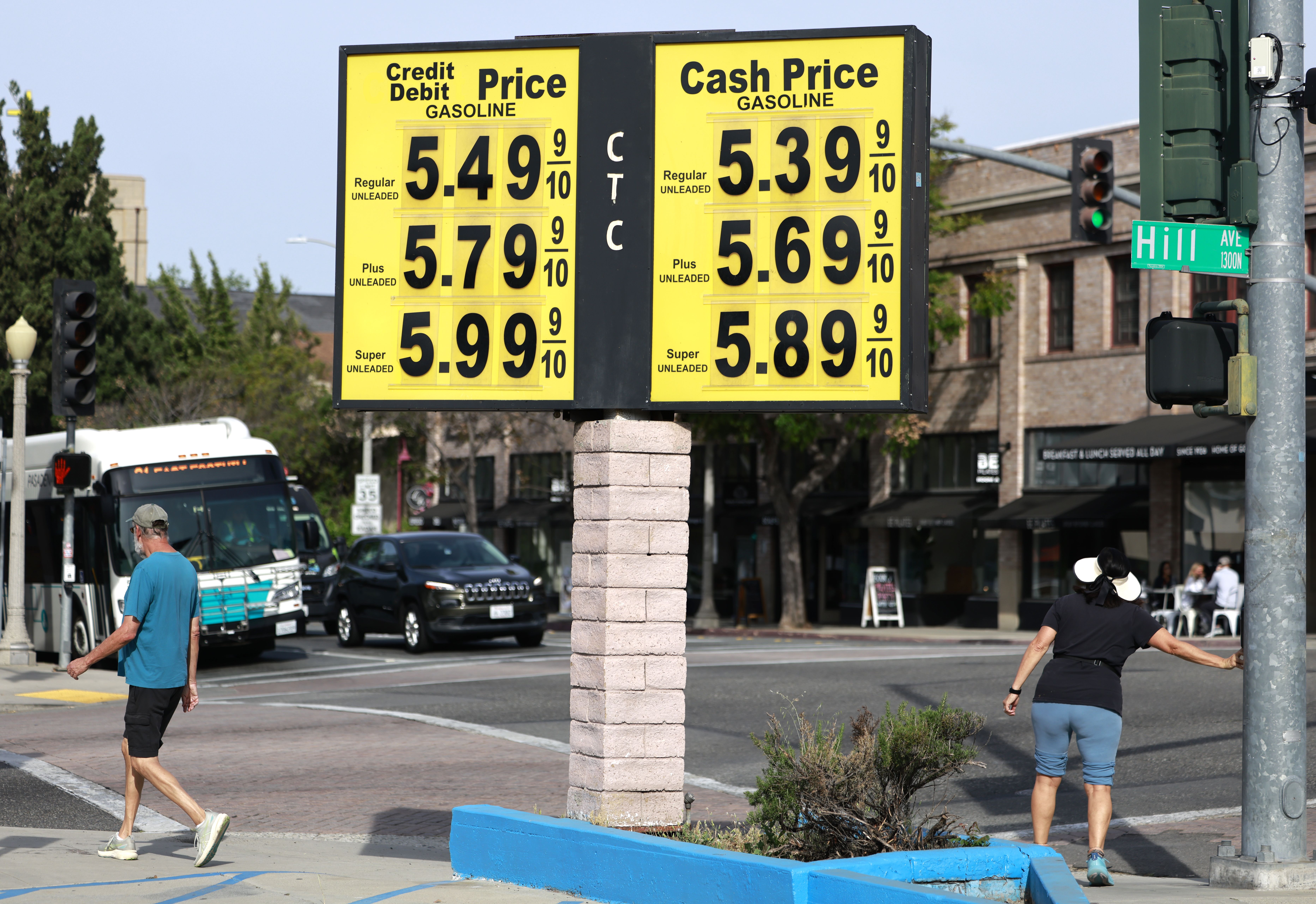 A gas station price board in Pasadena shows high fuel prices, with cars and pumps visible beneath the sign.